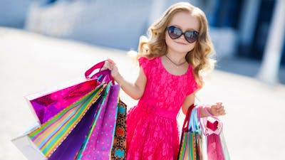 A young girl wearing sunglasses and holding shopping bags smiling for the camera at a market