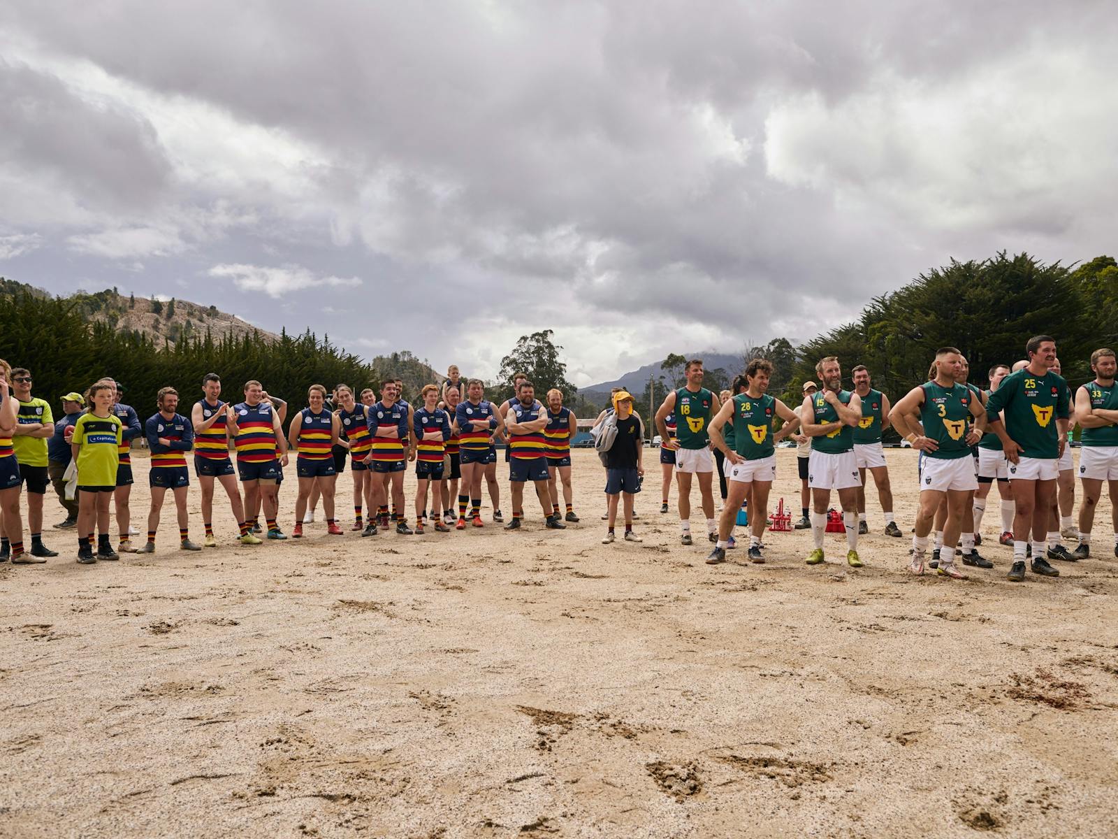Two football teams standing on a gravel oval.