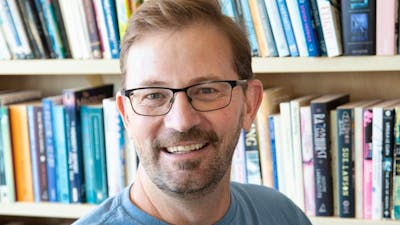 Man with glasses smiles in front of bookshelf