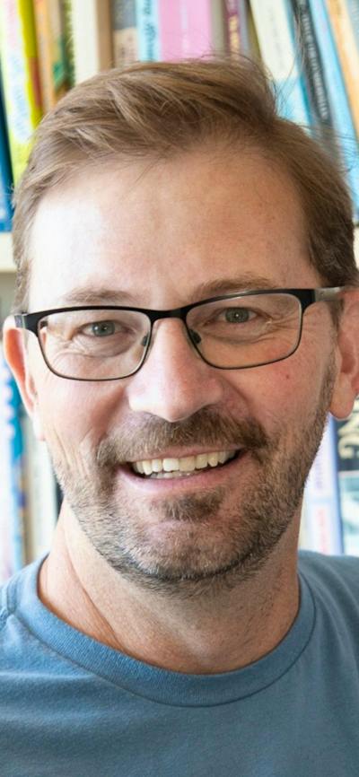 Man with glasses smiles in front of bookshelf