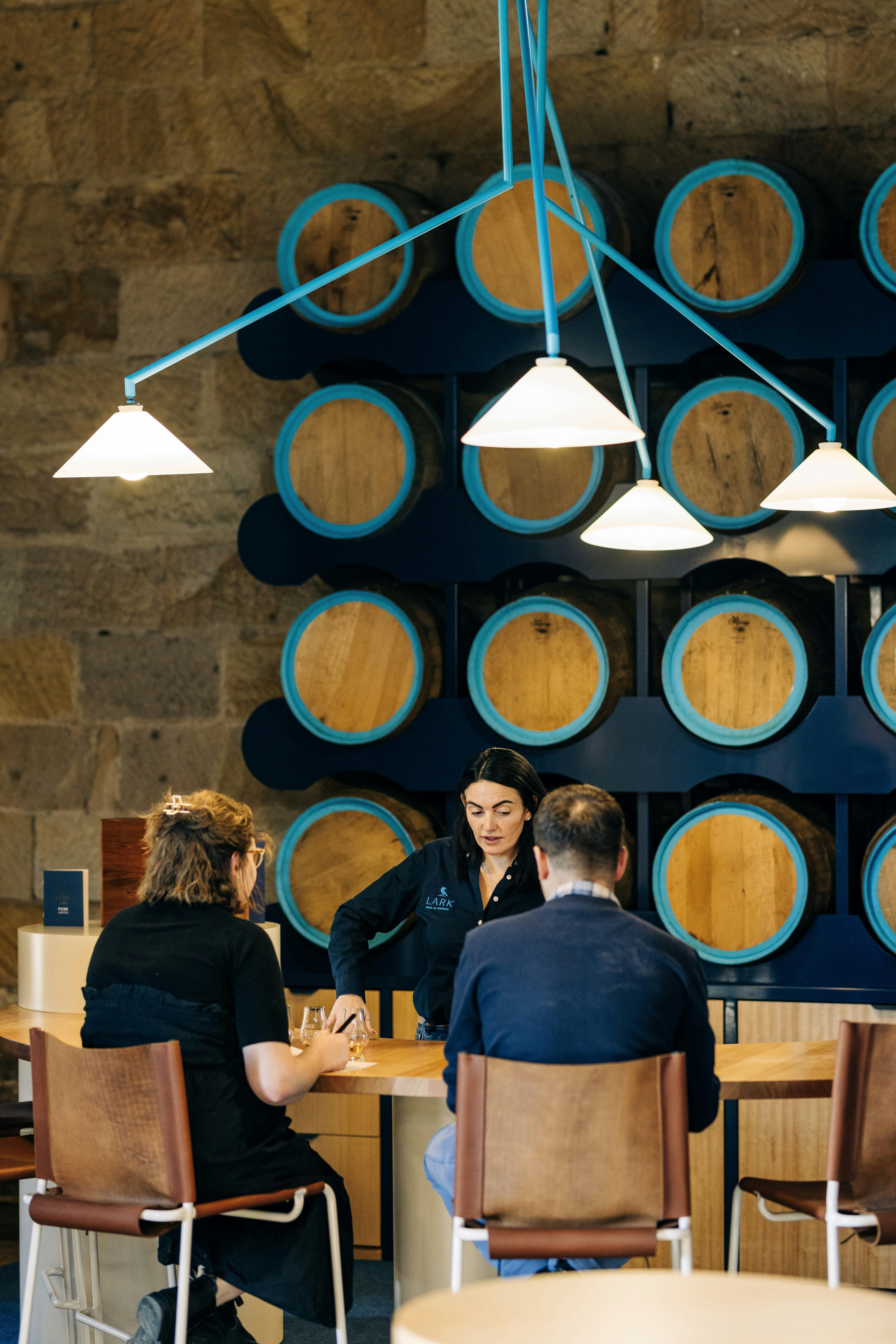 2 people seated at a high table being hosted by a tour guide for a whisky tasting and blending.