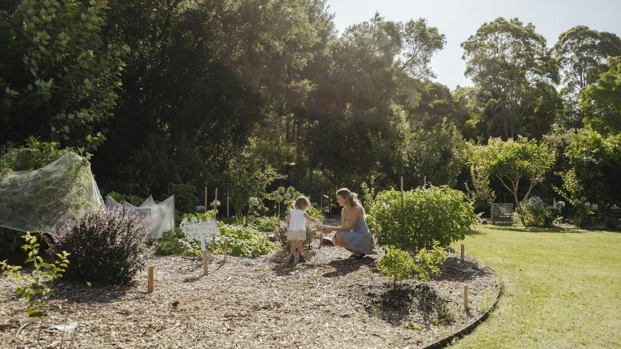 Image of mother and daughter crouched down in the abundant herb and vegetable garden.