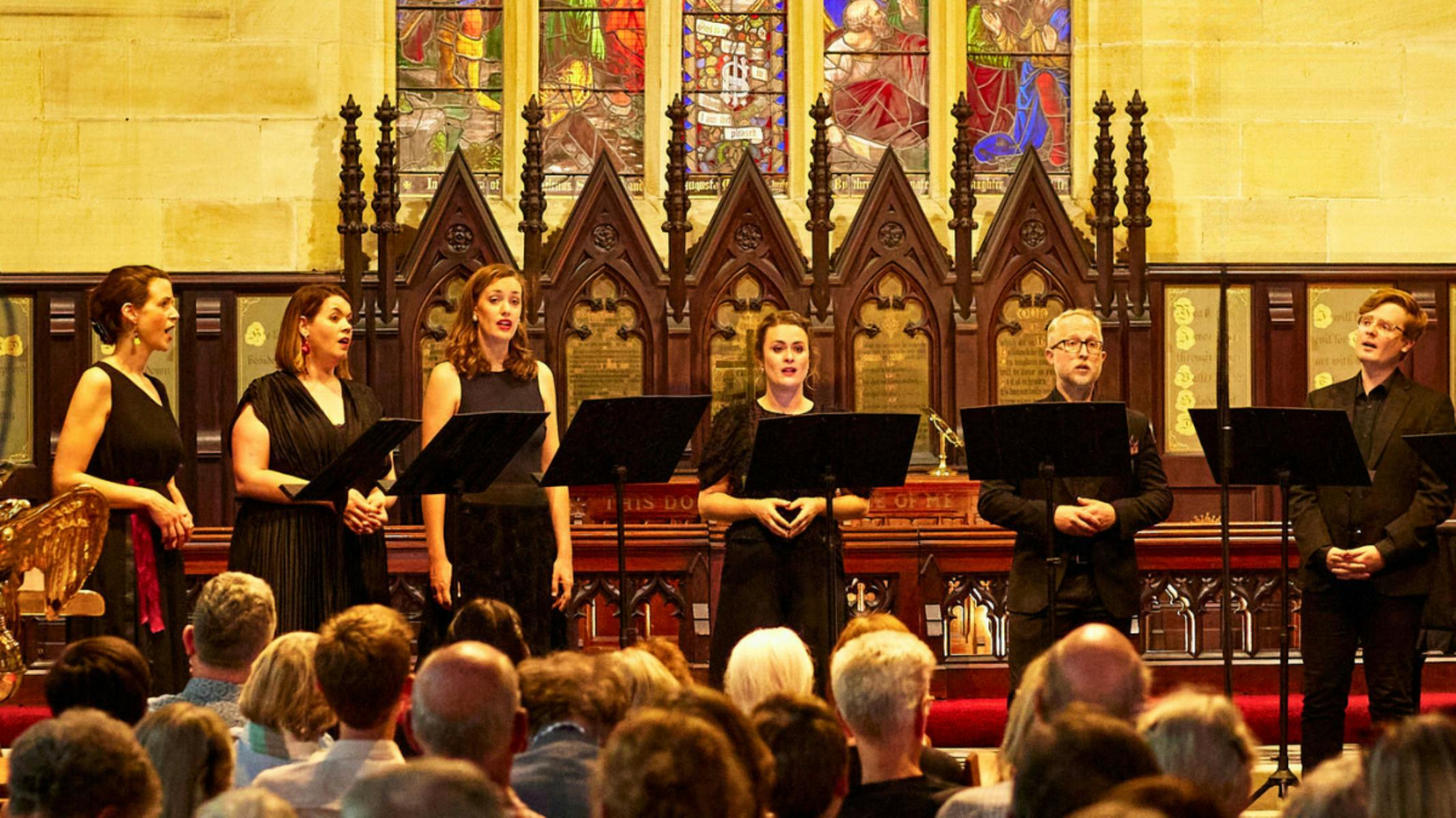 A group of choral singers standing at the altar of an ornate church singing.