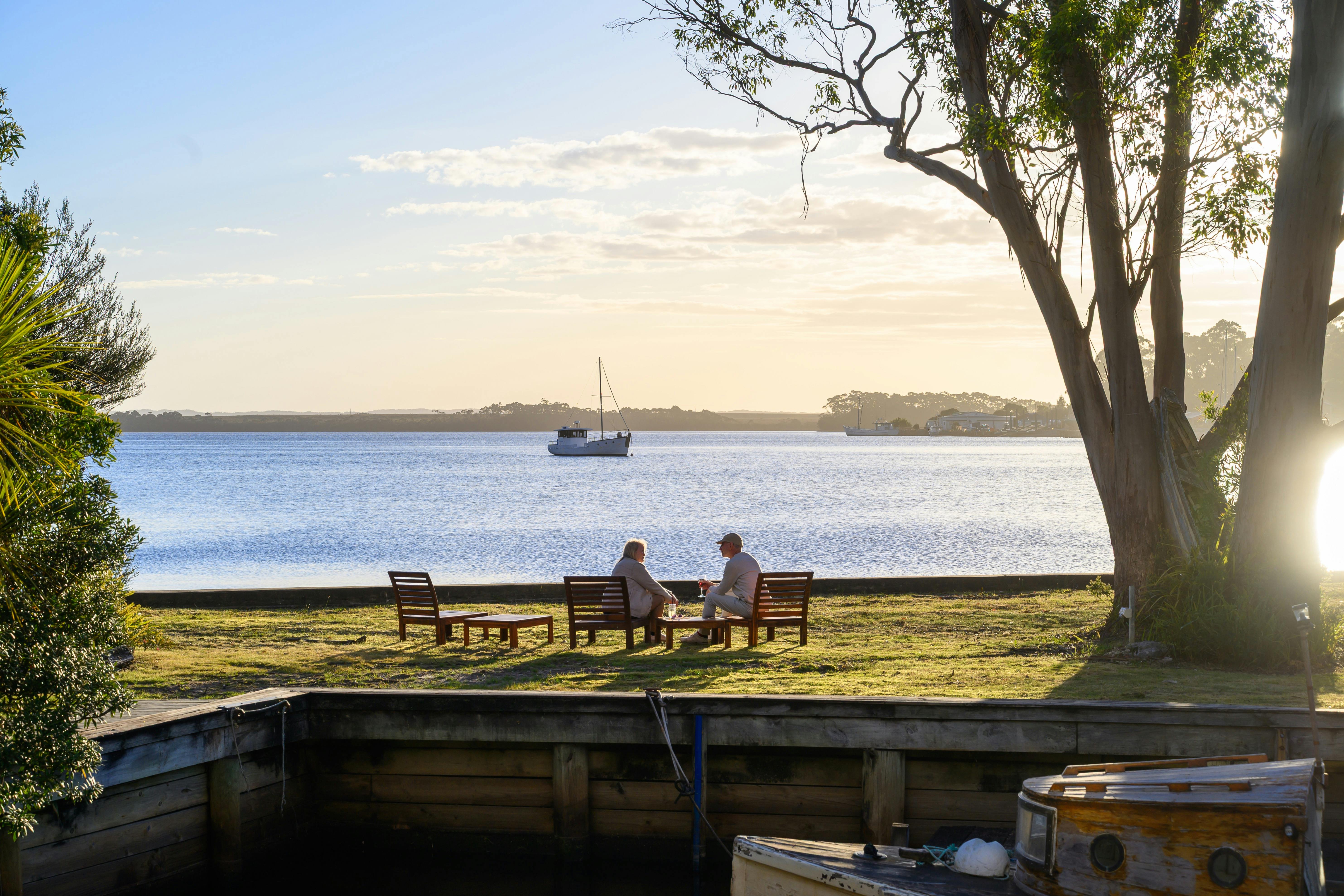 Couple sitting on the lawn with drinks with Macquarie Harbour in the background