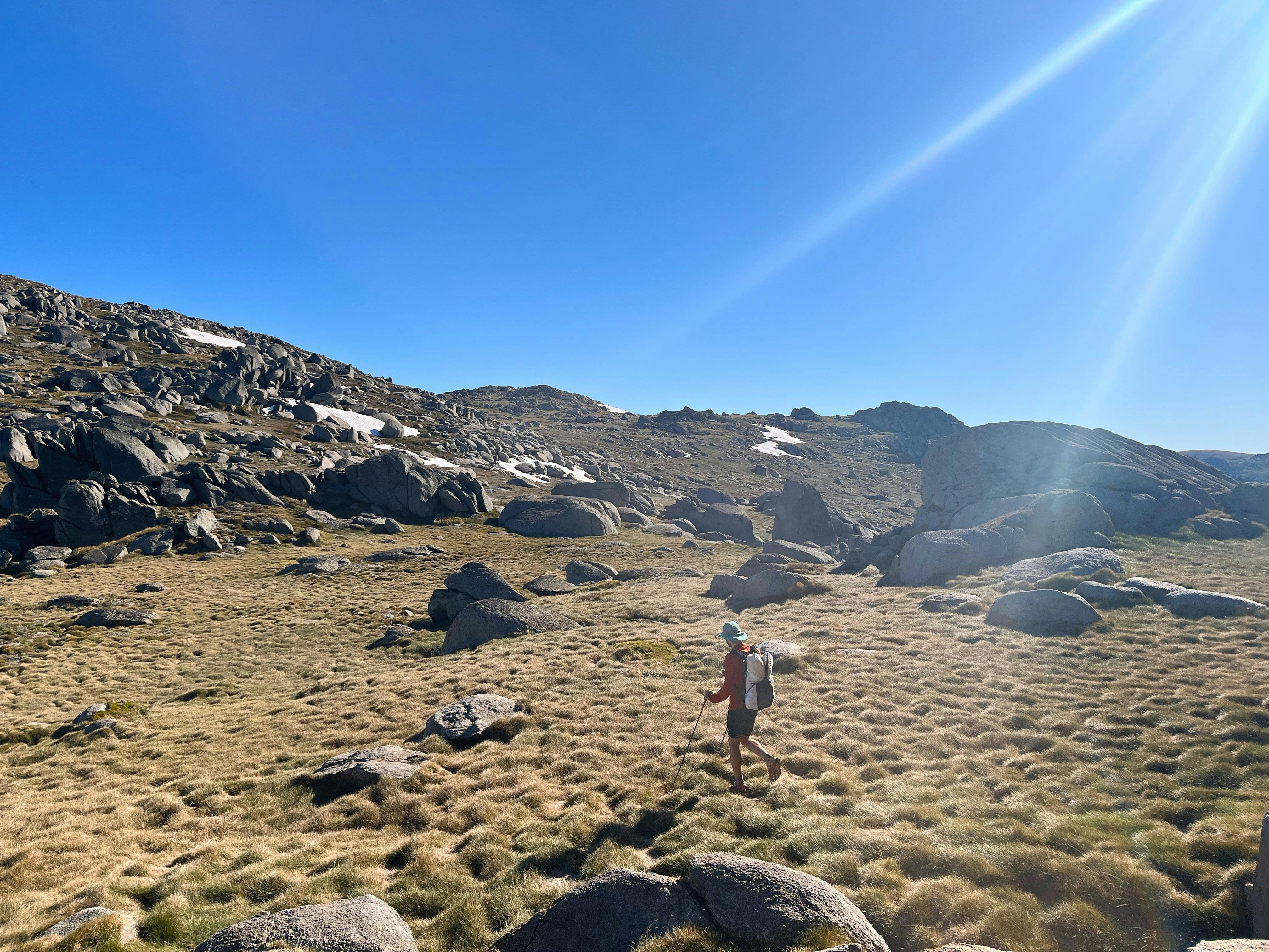 A hiker standing in open terrain with some snow in the background.