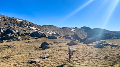 A hiker standing in open terrain with some snow in the background.