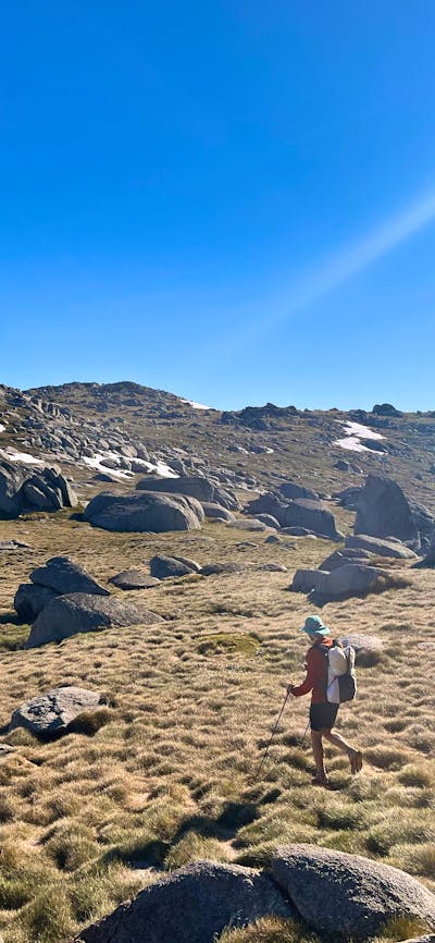 A hiker standing in open terrain with some snow in the background.