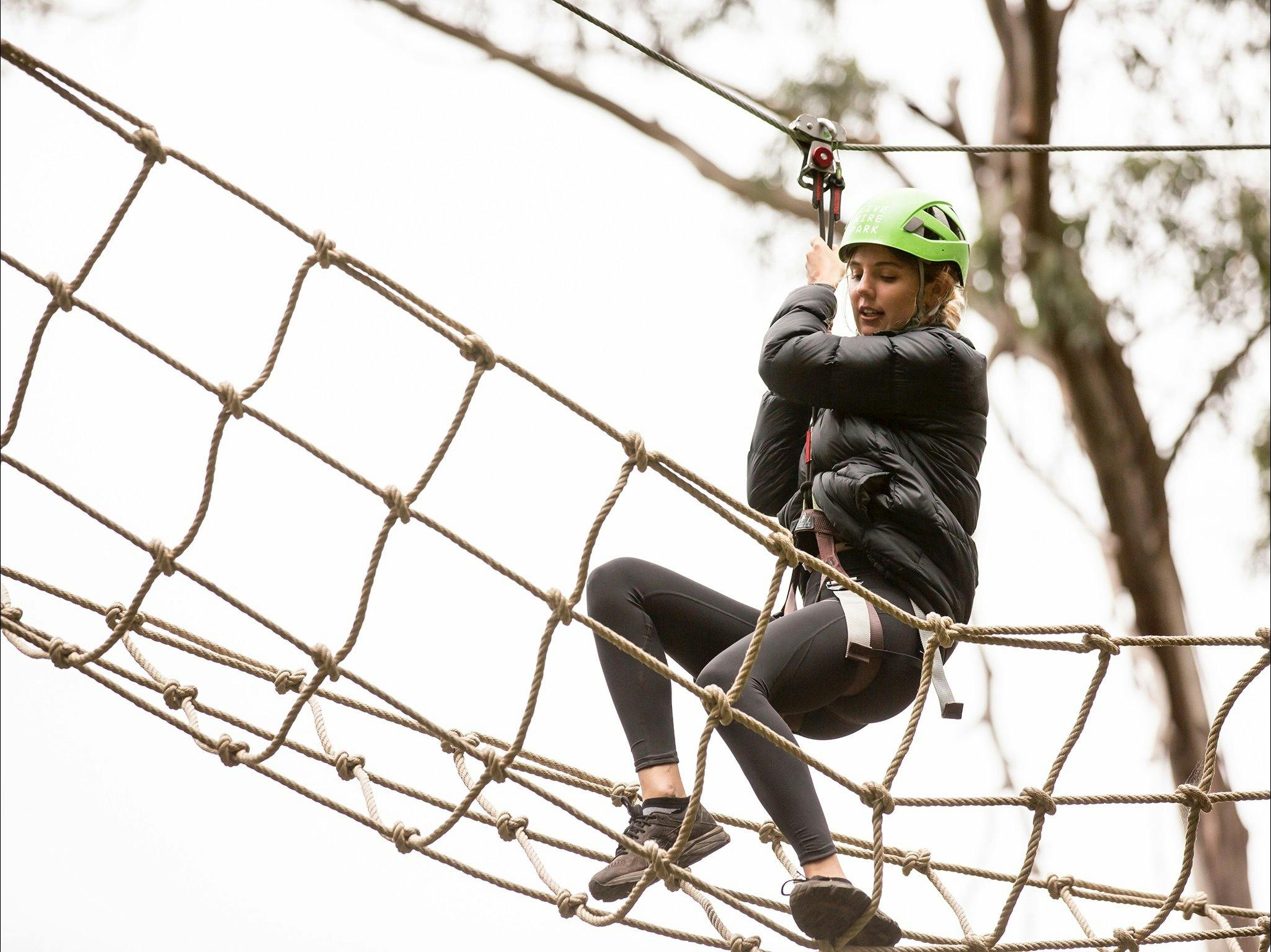Woman on a treetop adventure trail walking on a rope bridge