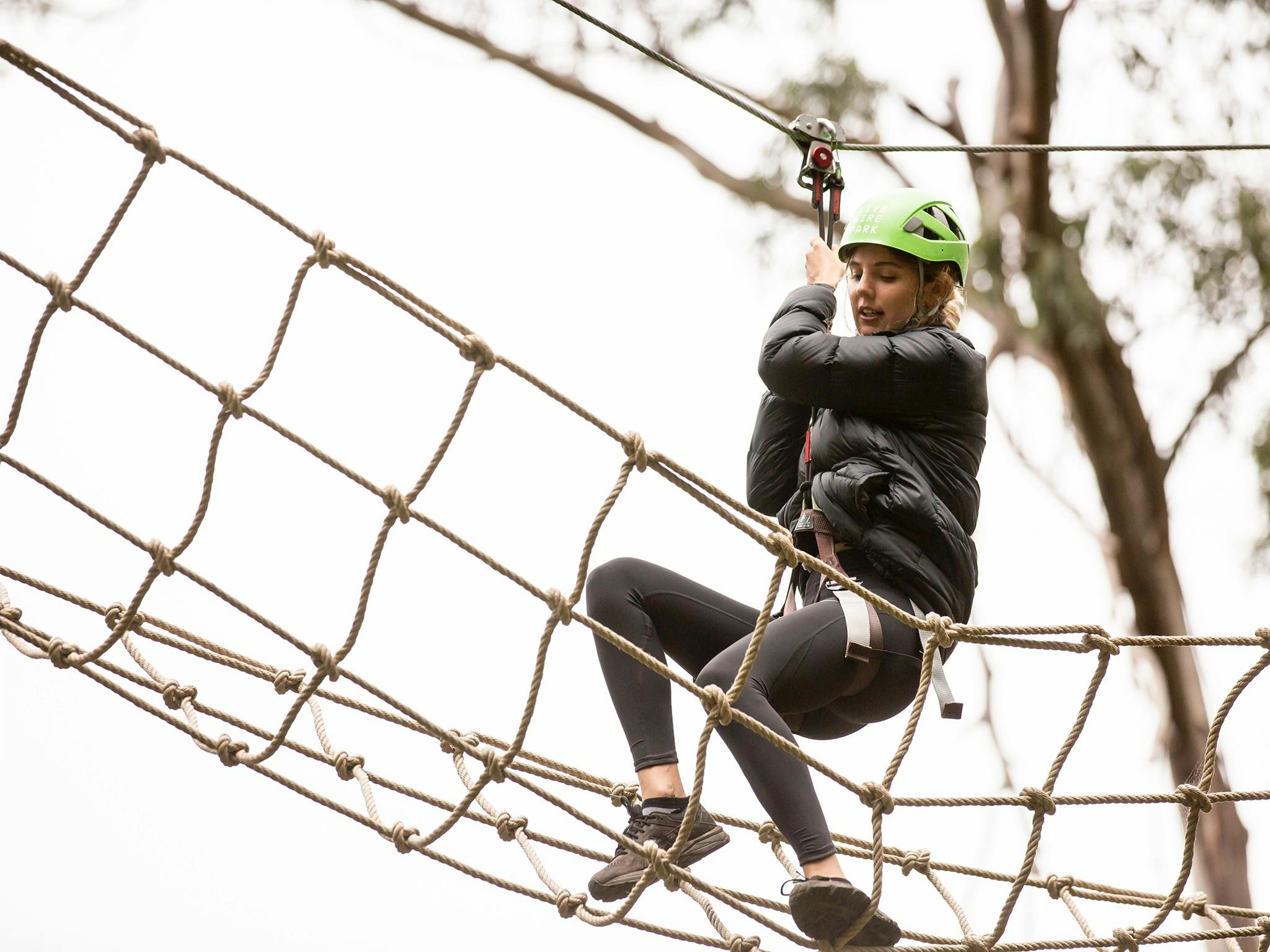 Woman on a treetop adventure trail walking on a rope bridge