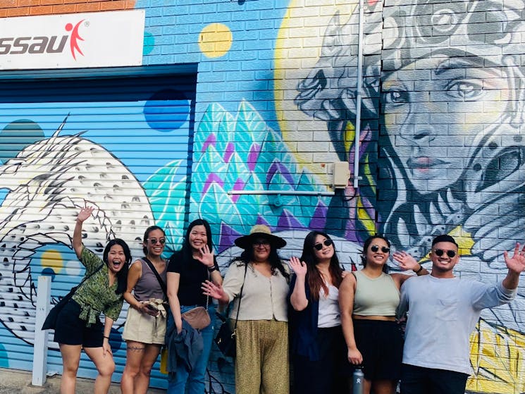 a group of friends waving in front of a Marrickville mural