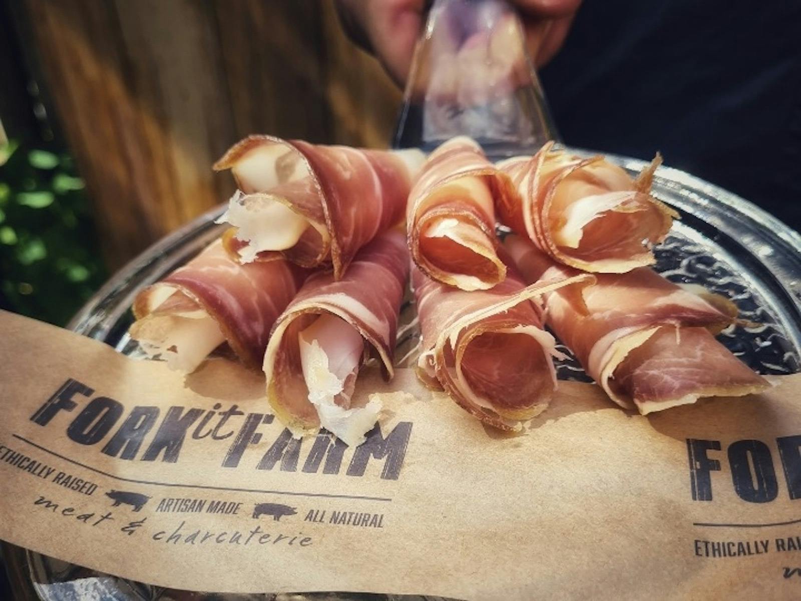 Close-up of rolled cured meat slices on rustic paper labeled "Fork it Farm."