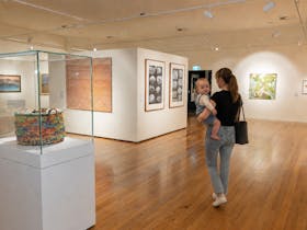 A young mother holds her baby on her hip as she walks through the art gallery