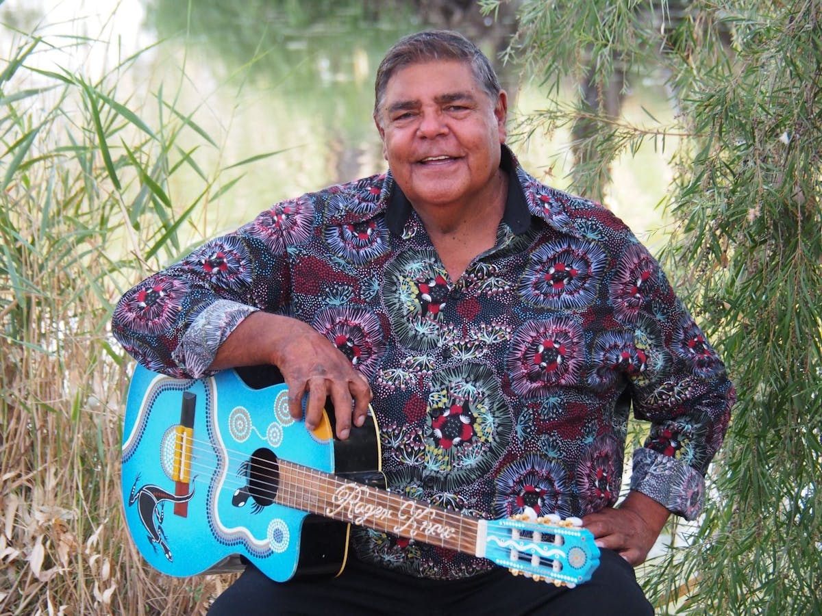 Image of Roger Knox holding blue guitar and smiling at camera.