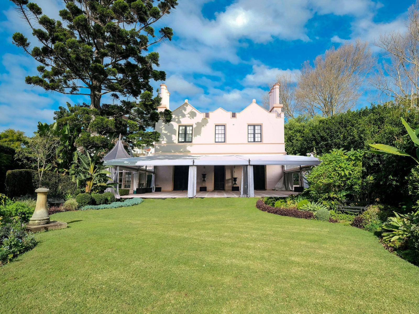 A grand white house in Gothic Revival style sits surrounded by gardens.