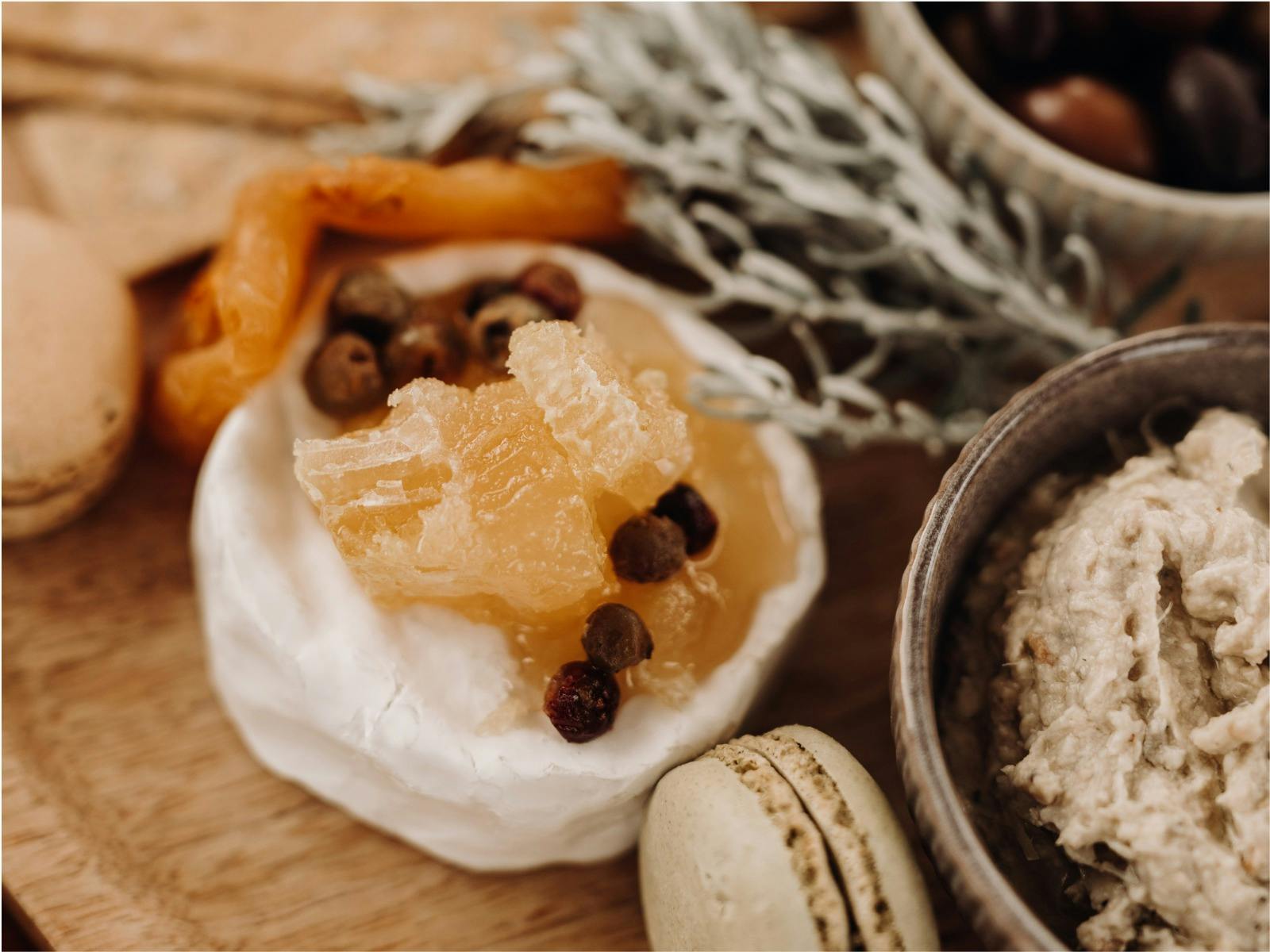 Close-up of a gourmet platter with cheese, honeycomb, macarons, and a dip, garnished with herbs.
