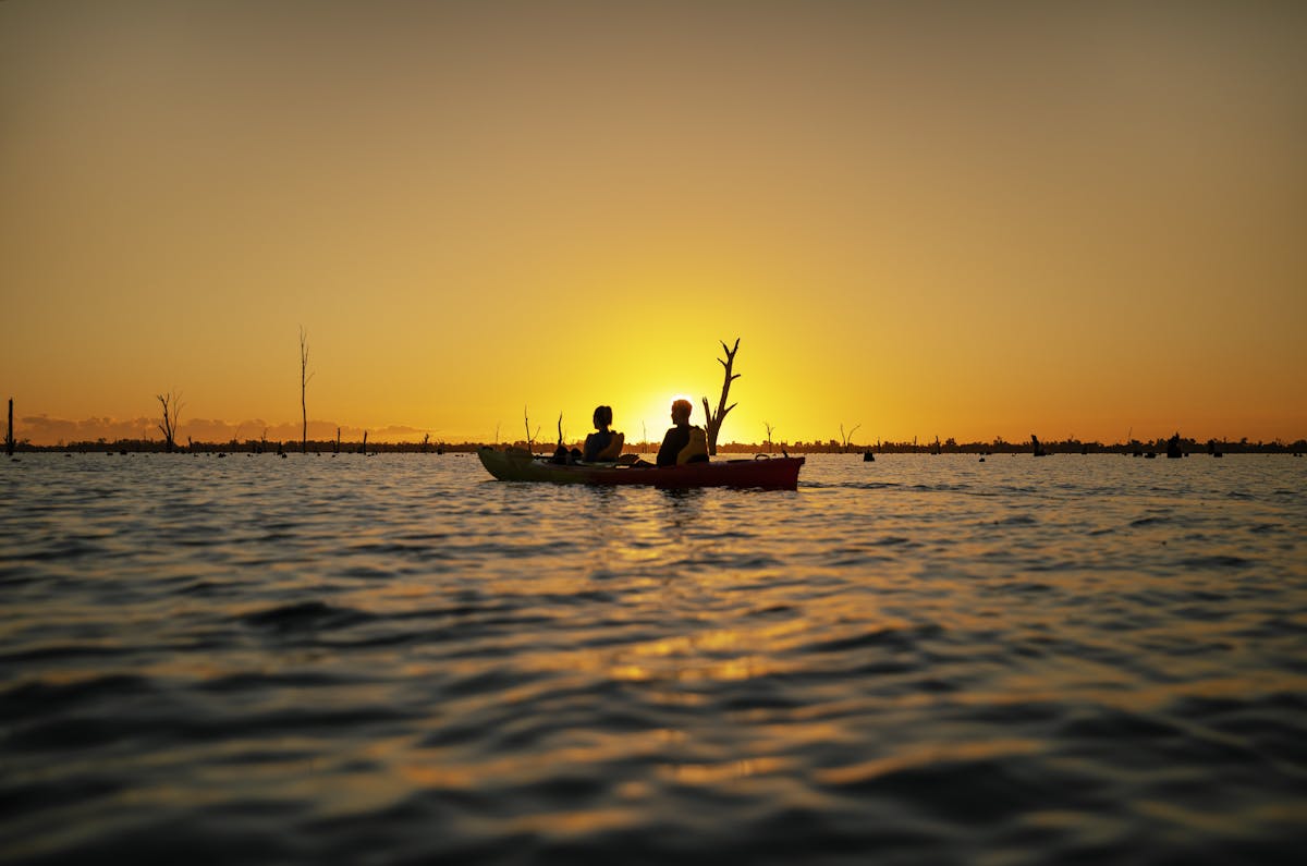 Kayakers sitting on lake mulwala with stunning orange sunset behind them