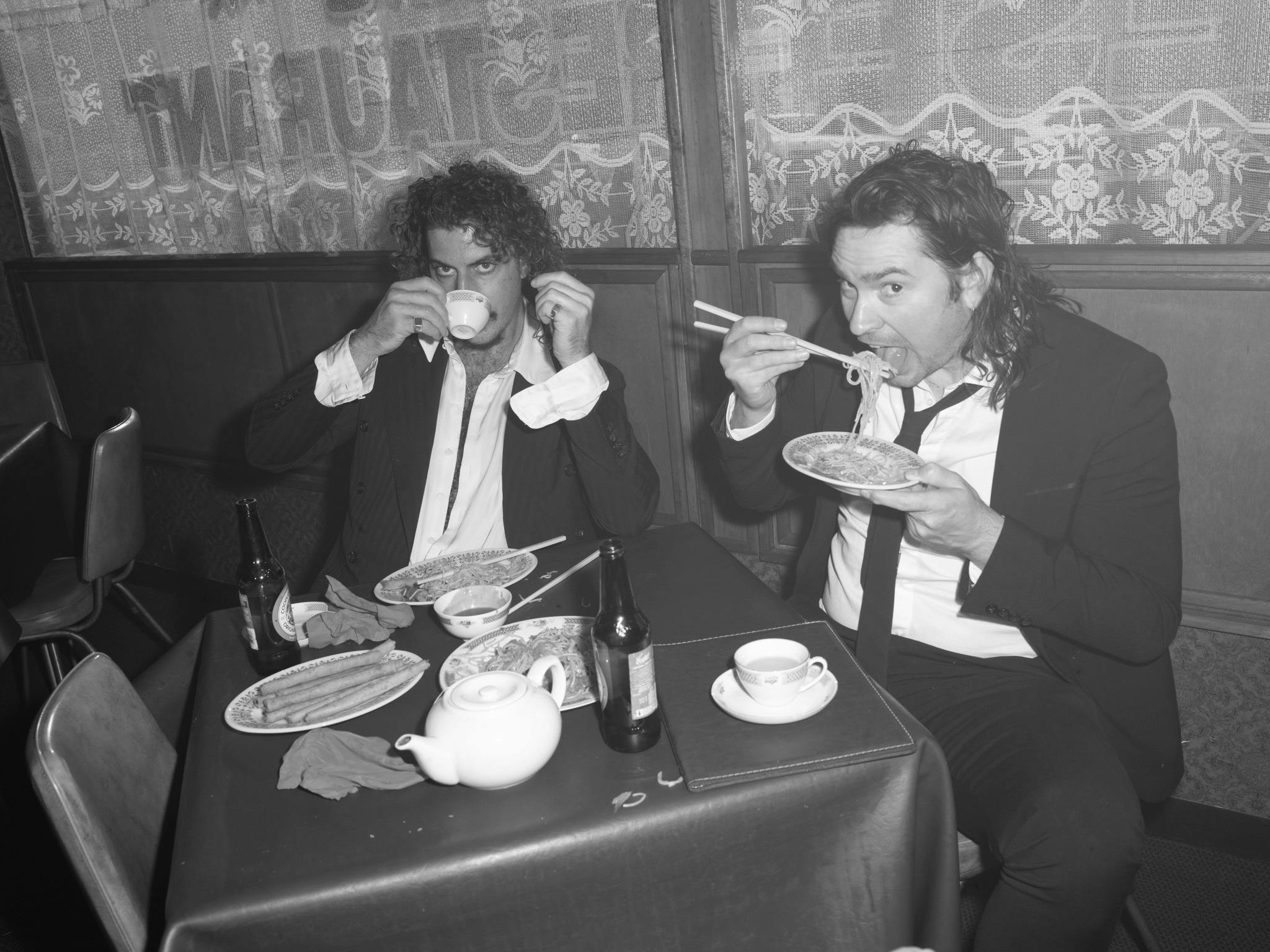 Peking Duk duo, Adam hyde having a sip of tea and Reuben Styles eating ramen at a restaurant.