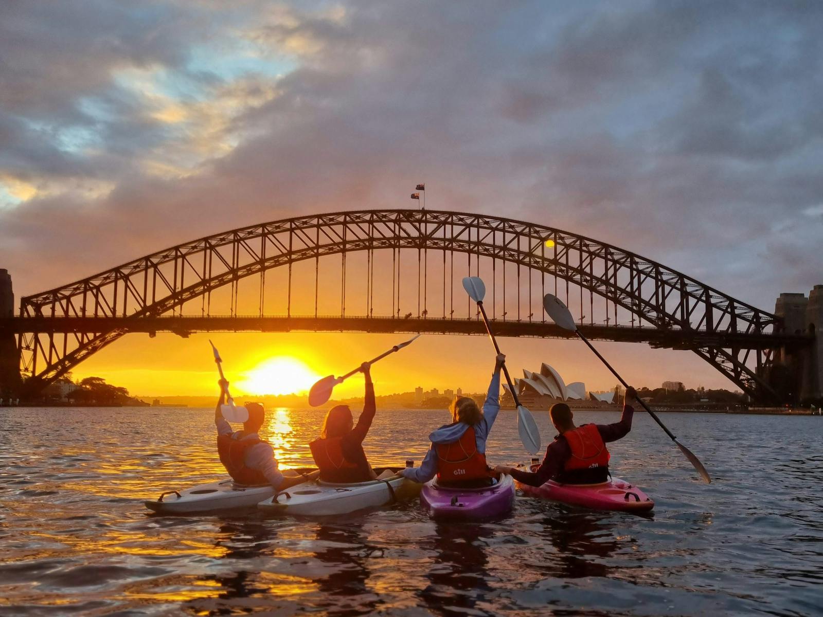 Four kayakers celebrating a beautiful sunrise on sydney harbour in front of sydney harbour bridge