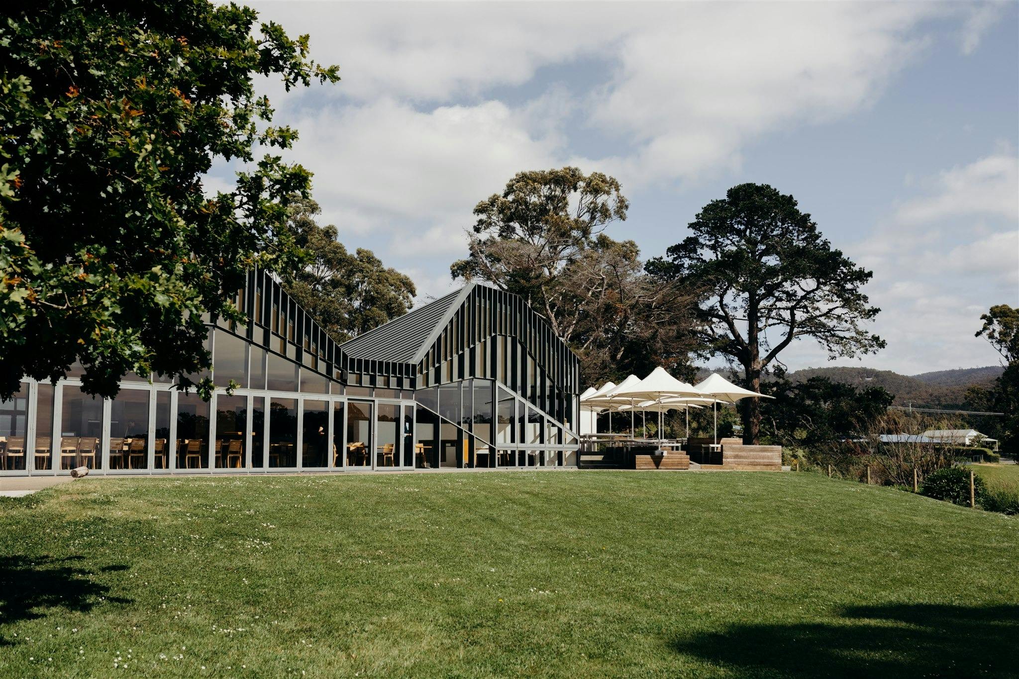 External view of Peppermint Bay restaurant. Large glass windows. Green lawn. Architectural angles.