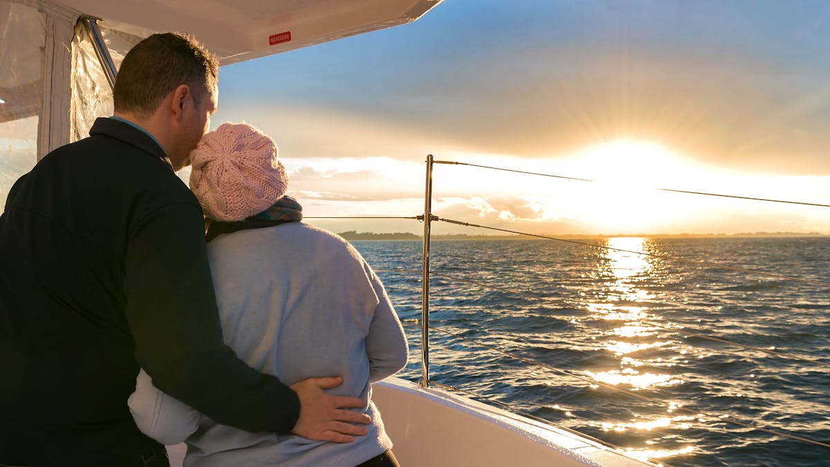 A couple enjoys the view of the sun setting across the bay from the comfort of the catamaran.