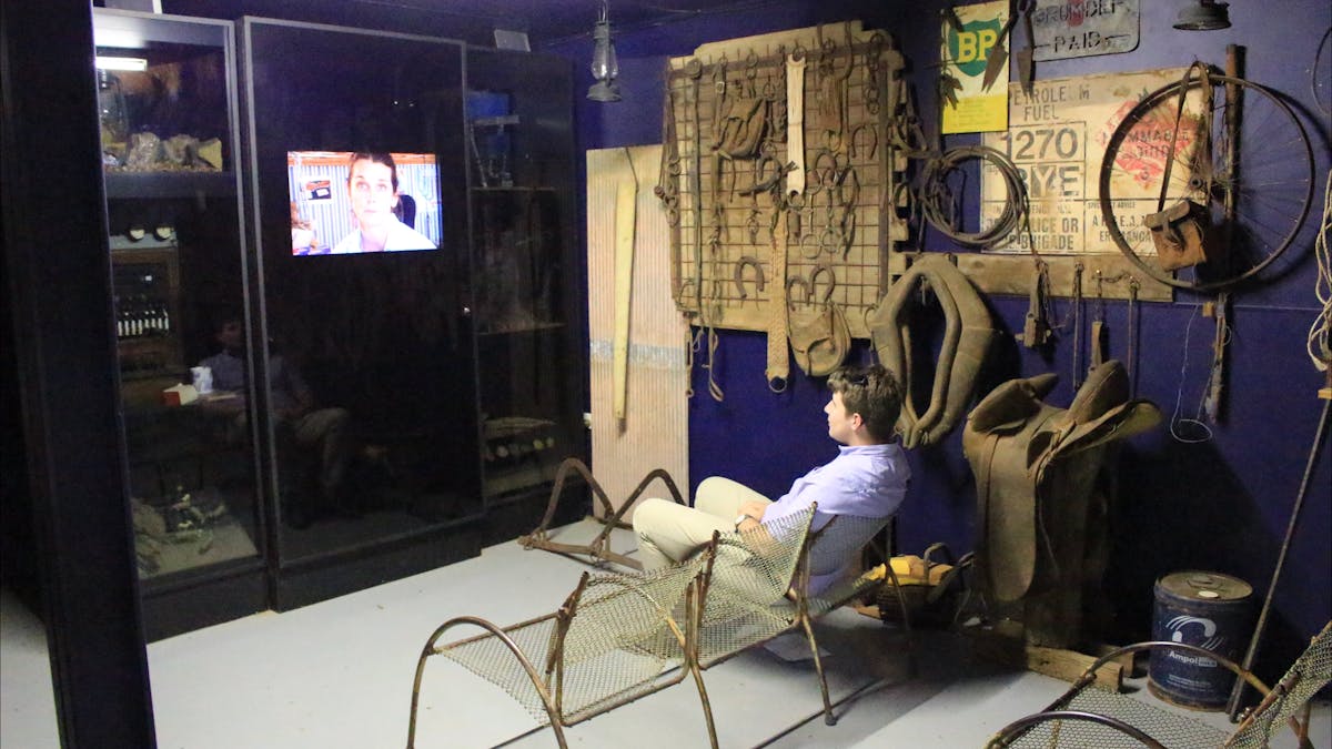 Person sitting in chair facing the screen, woman on the screen, eclectic old styling