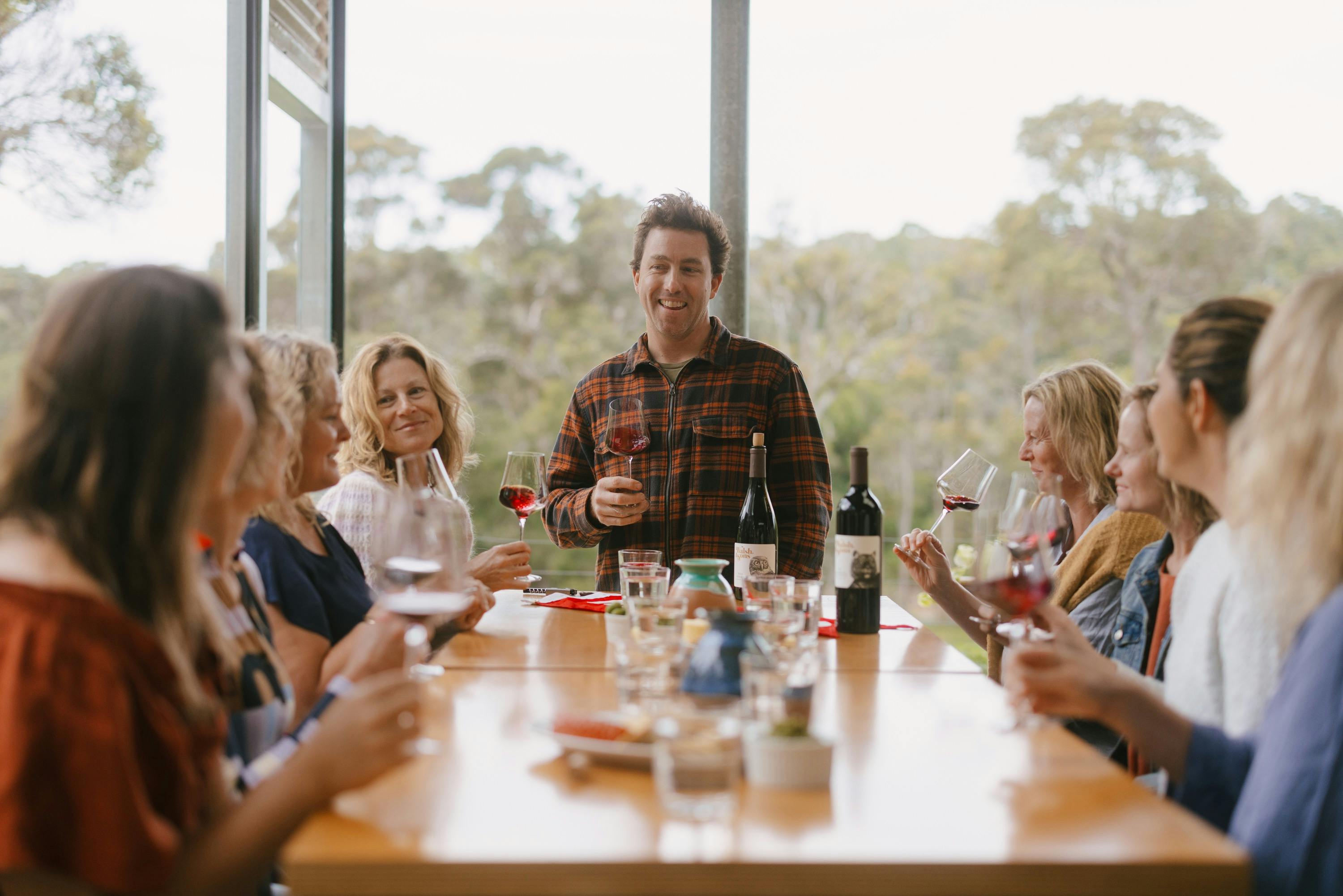 ladies sit around a table swirling wine in their glasses laughing with a winemaker