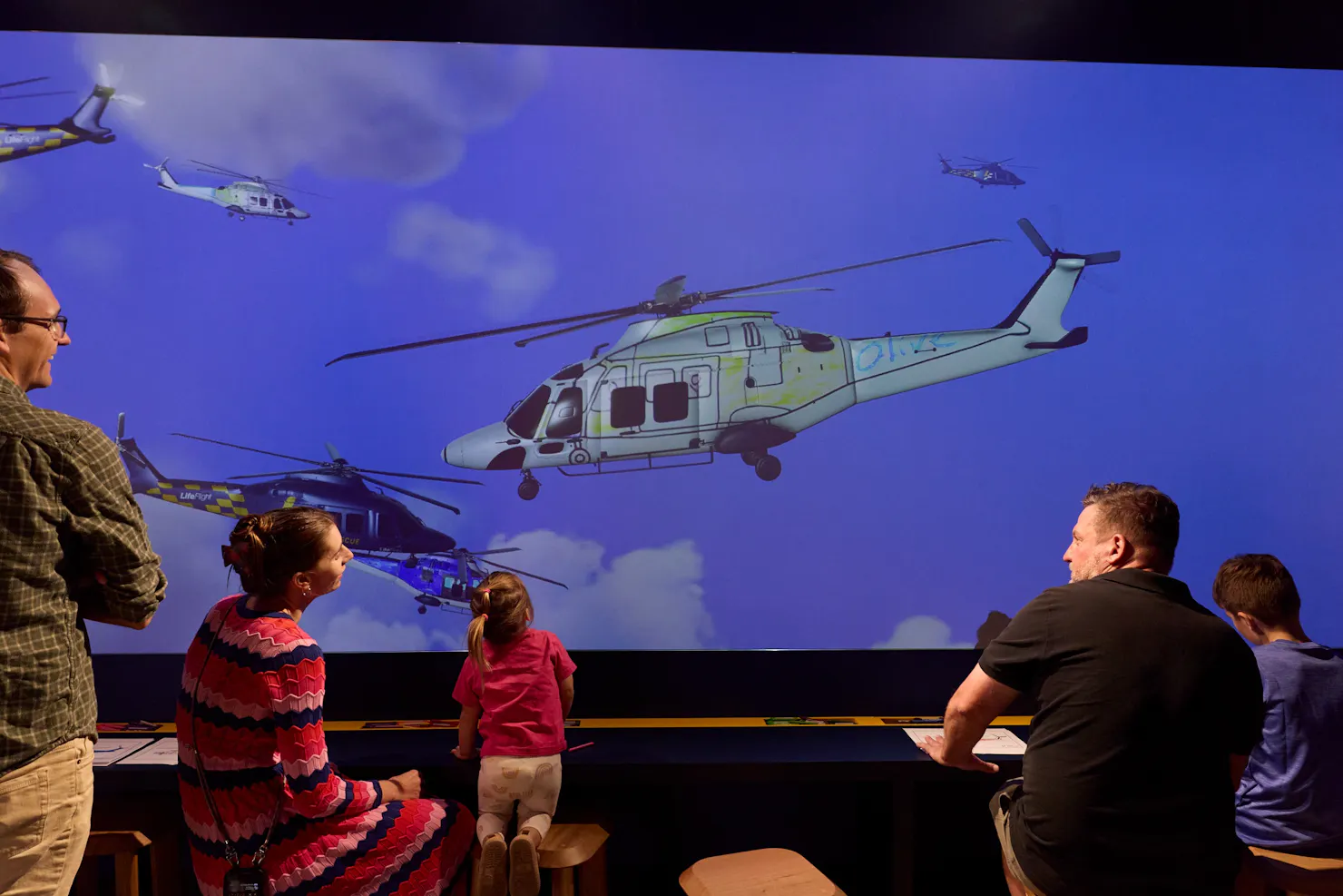 Family watching helicopter drawing fly across projection screen