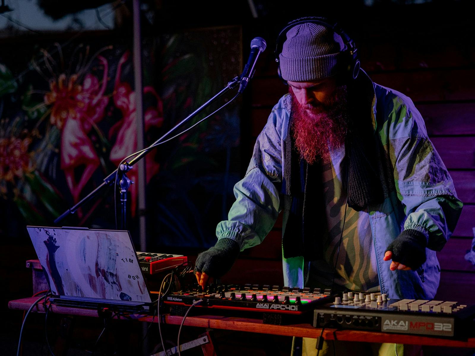 A man is flooded with purple light while he adjusts the sound board in front of him.