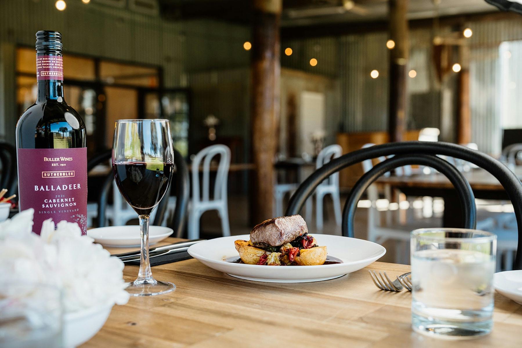 A main meal of Lamb Back Strap served on the table with a bottle of Balladeer Cabernet Sauvignon