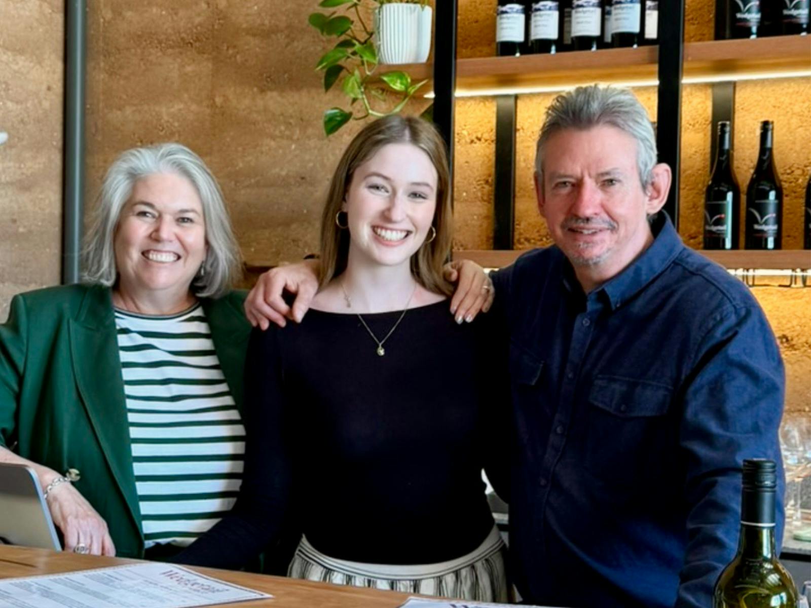 Parents and a young adult daughter embracing by a bar at a cellar door