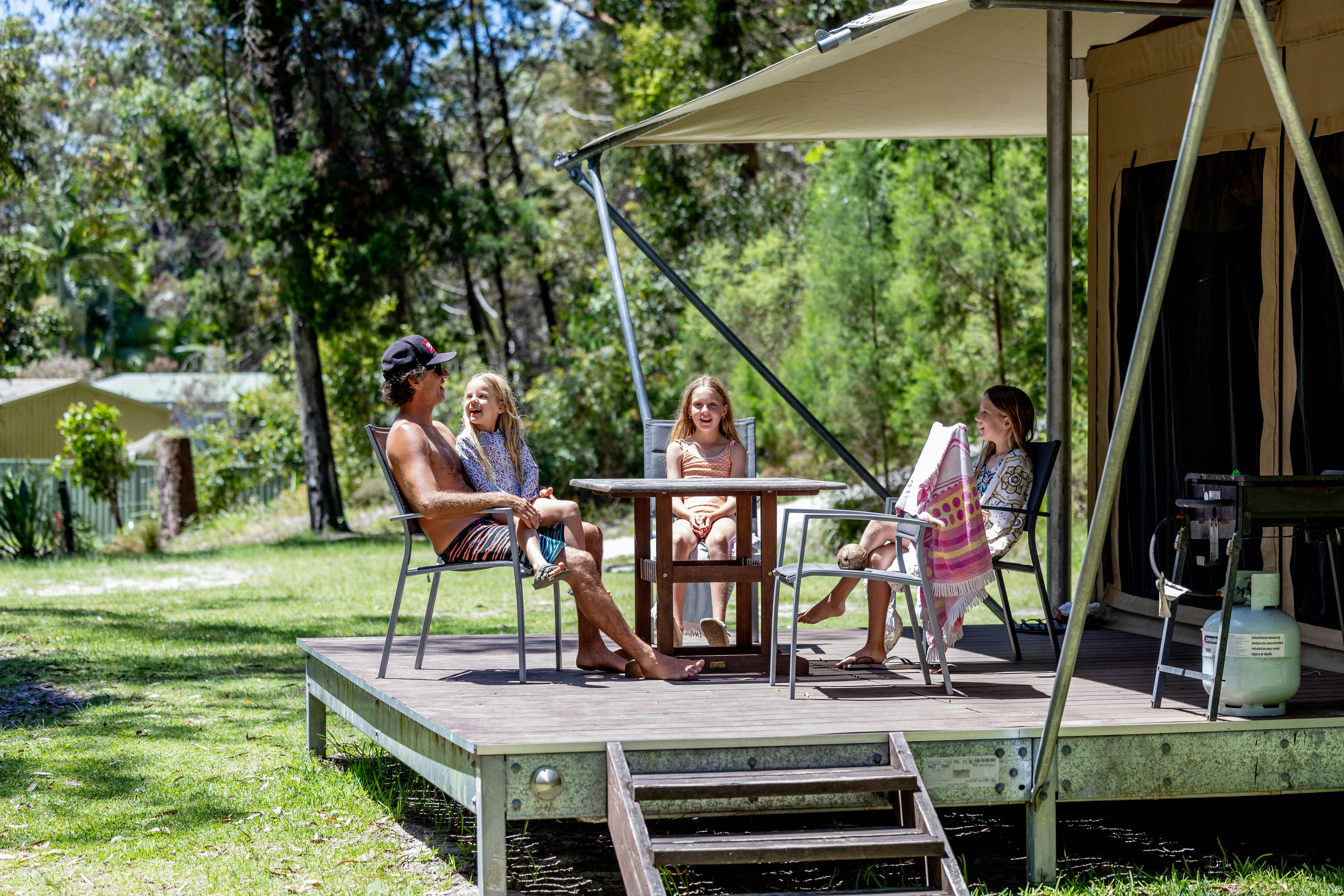 デッキの屋外ダイニングテーブルの周りに座っている笑顔の家族