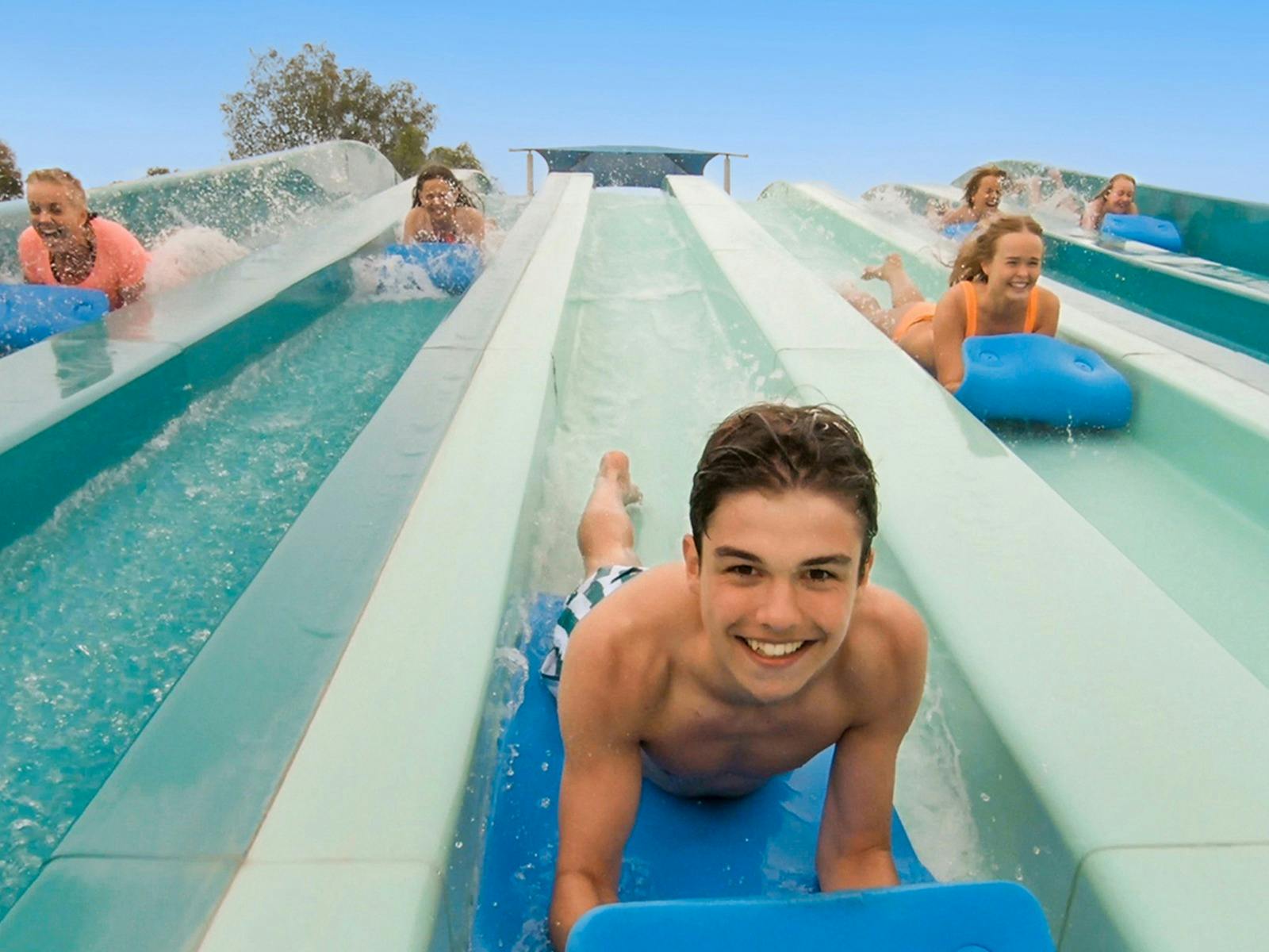 A boy smiling at the camera while going down the Aqua Racer water slide at Adventure Park