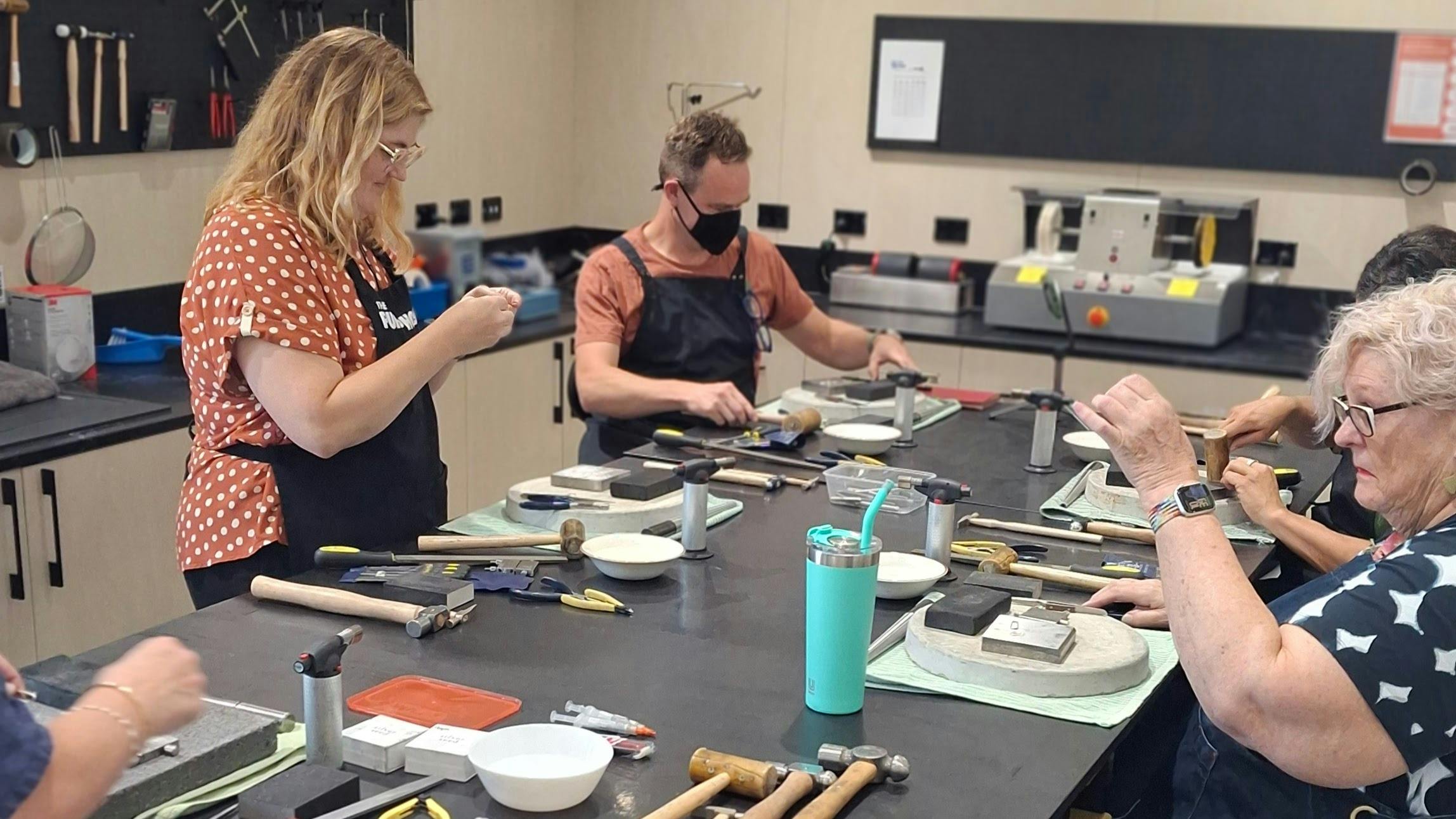 people using silversmithing tools to make jewellery