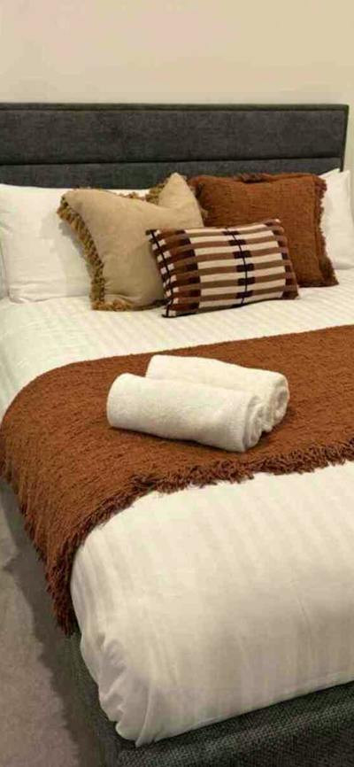 Bedroom with grey fabric headboard, white linens, rust-orange throw blanket, and black bedside table