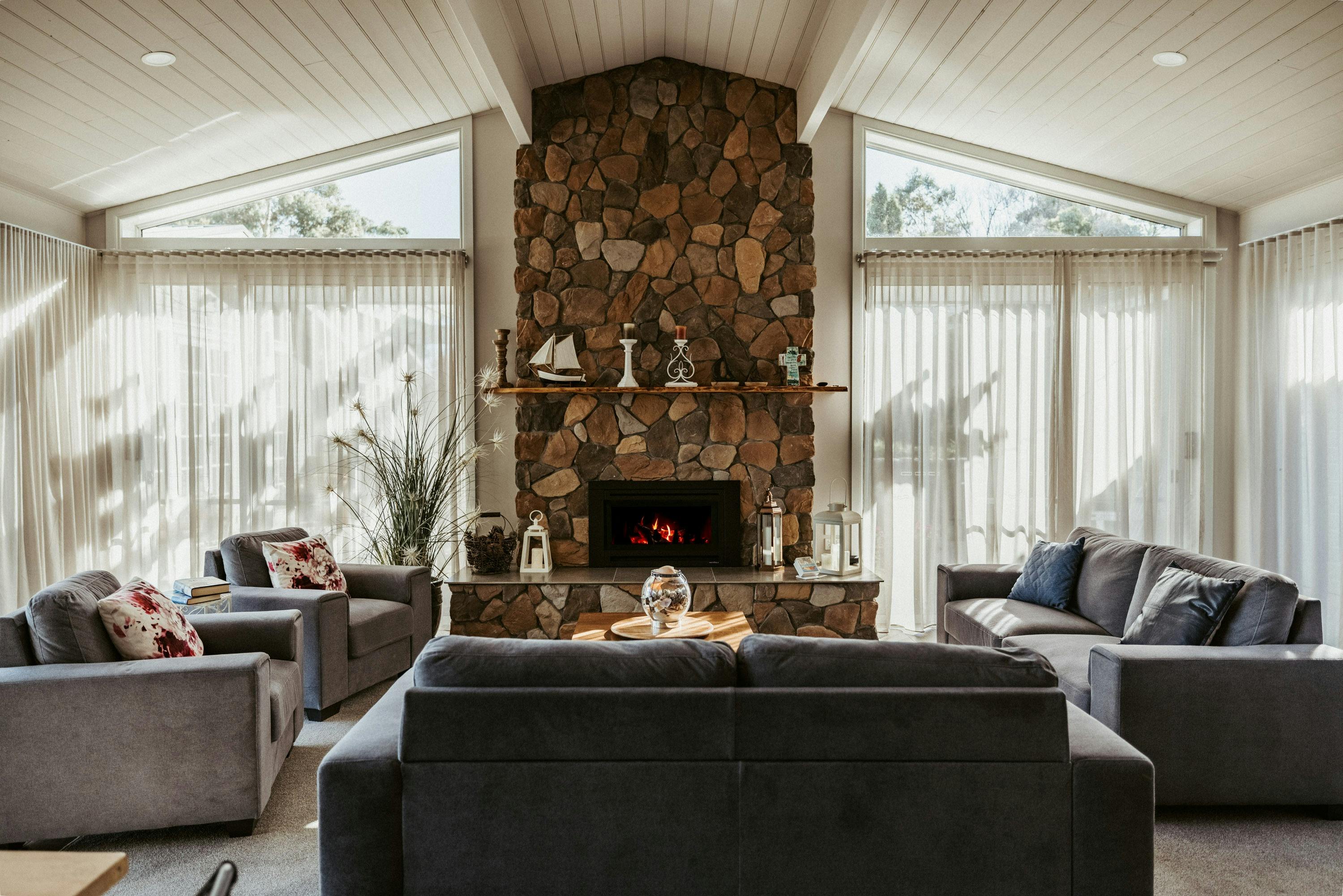 The living room offers plenty of seating, a cosy gas fireplace heater, and motorised blinds.