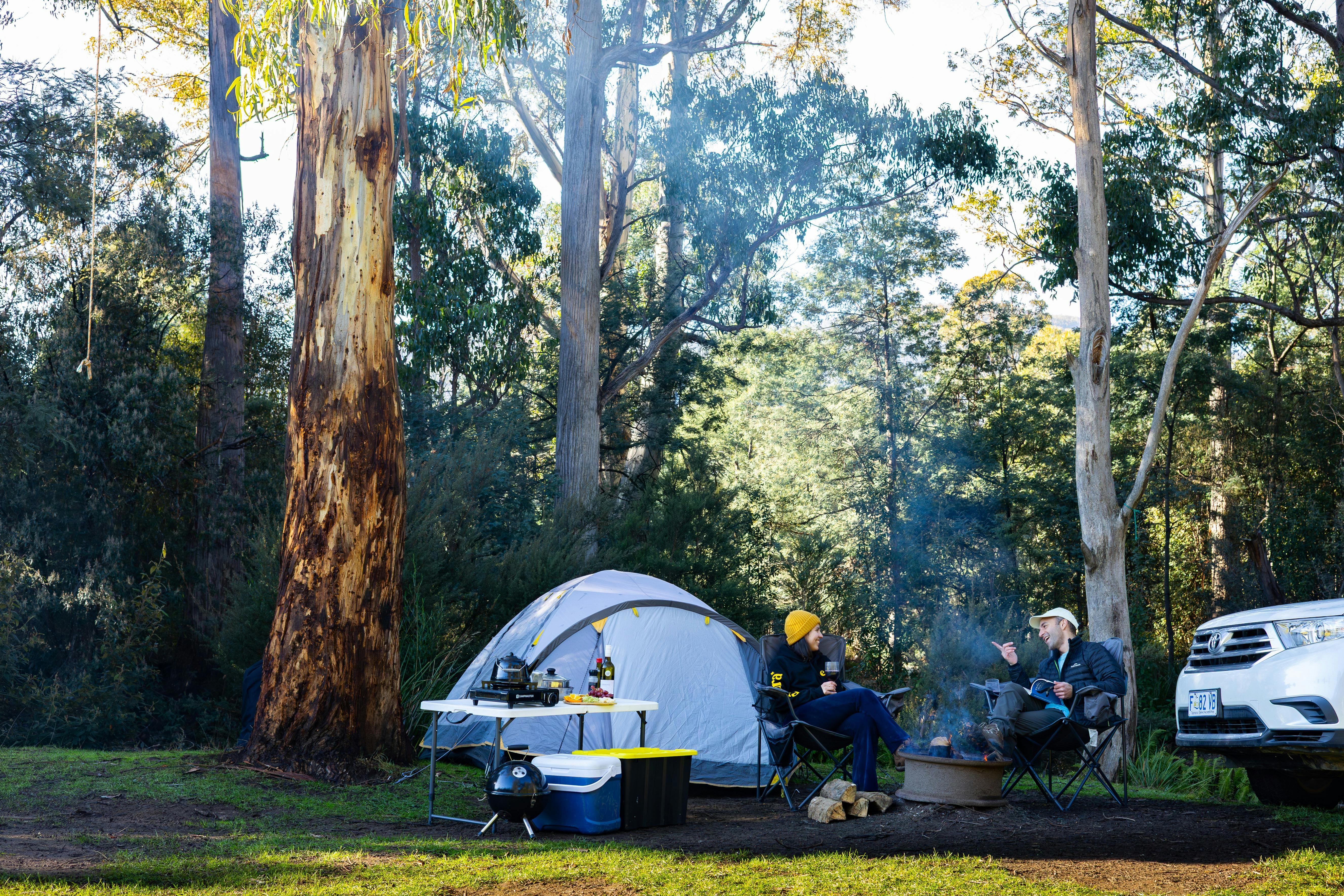 Two people sitting on their camping spot enjoying a nice time next to the fire