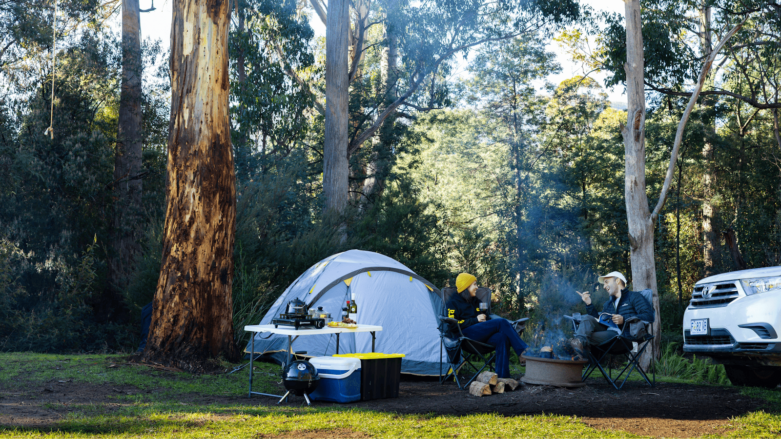 Two people sitting on their camping spot enjoying a nice time next to the fire