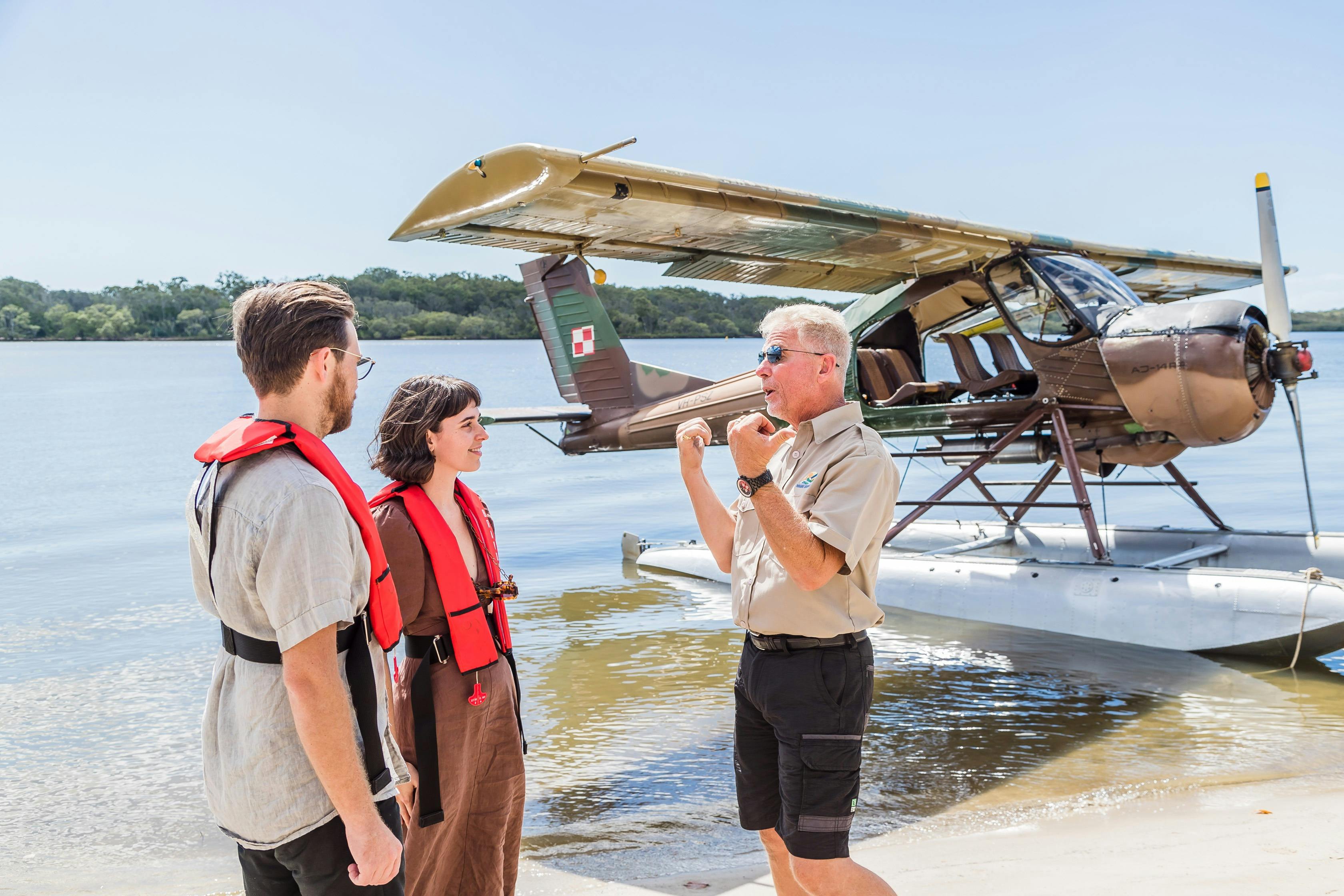 Young couple talk to pilot on the beach with seaplane in background