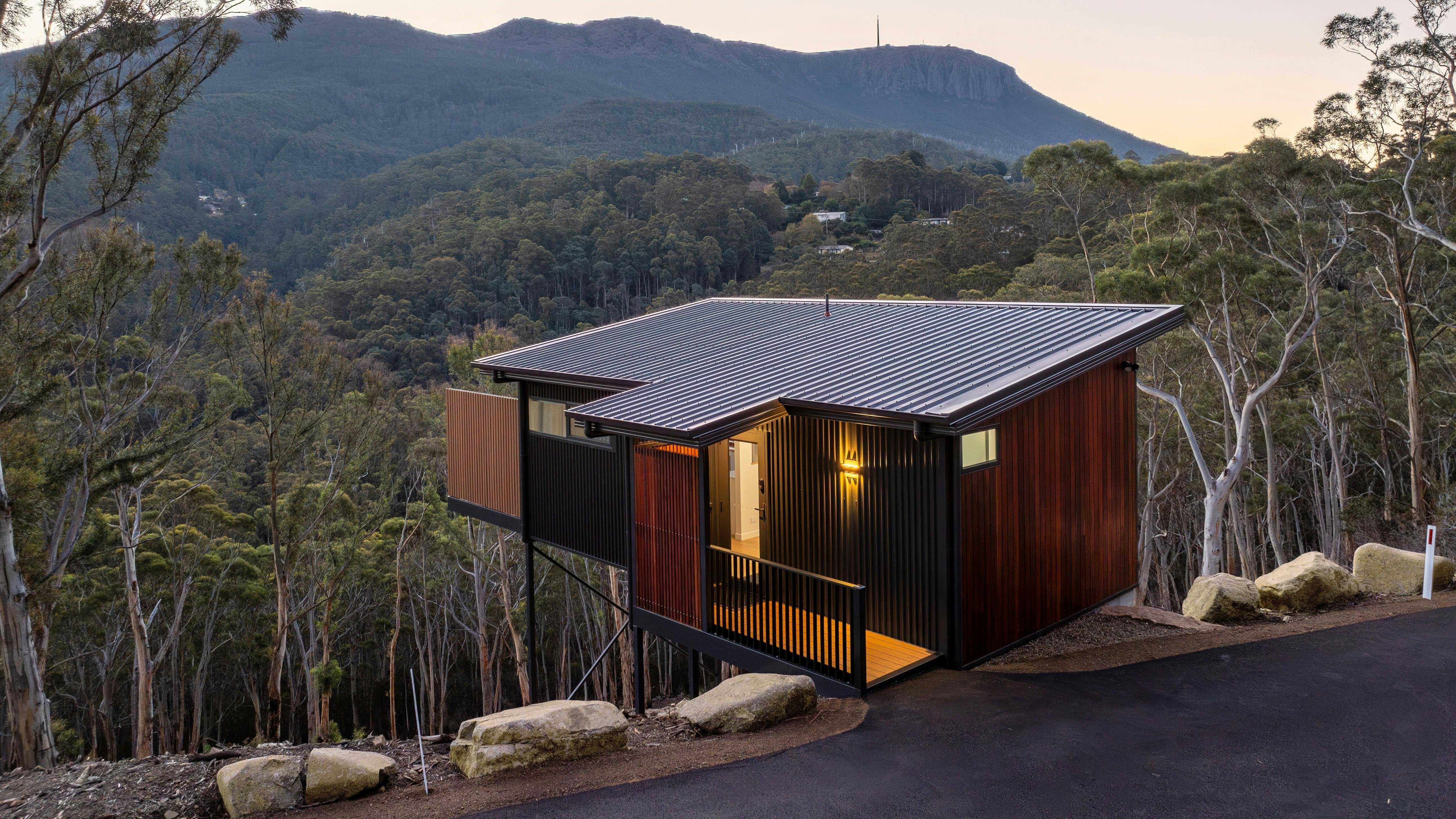 Modern cabin nestled in a hill overlooking trees with kunanyi / Mt Wellington filling the view