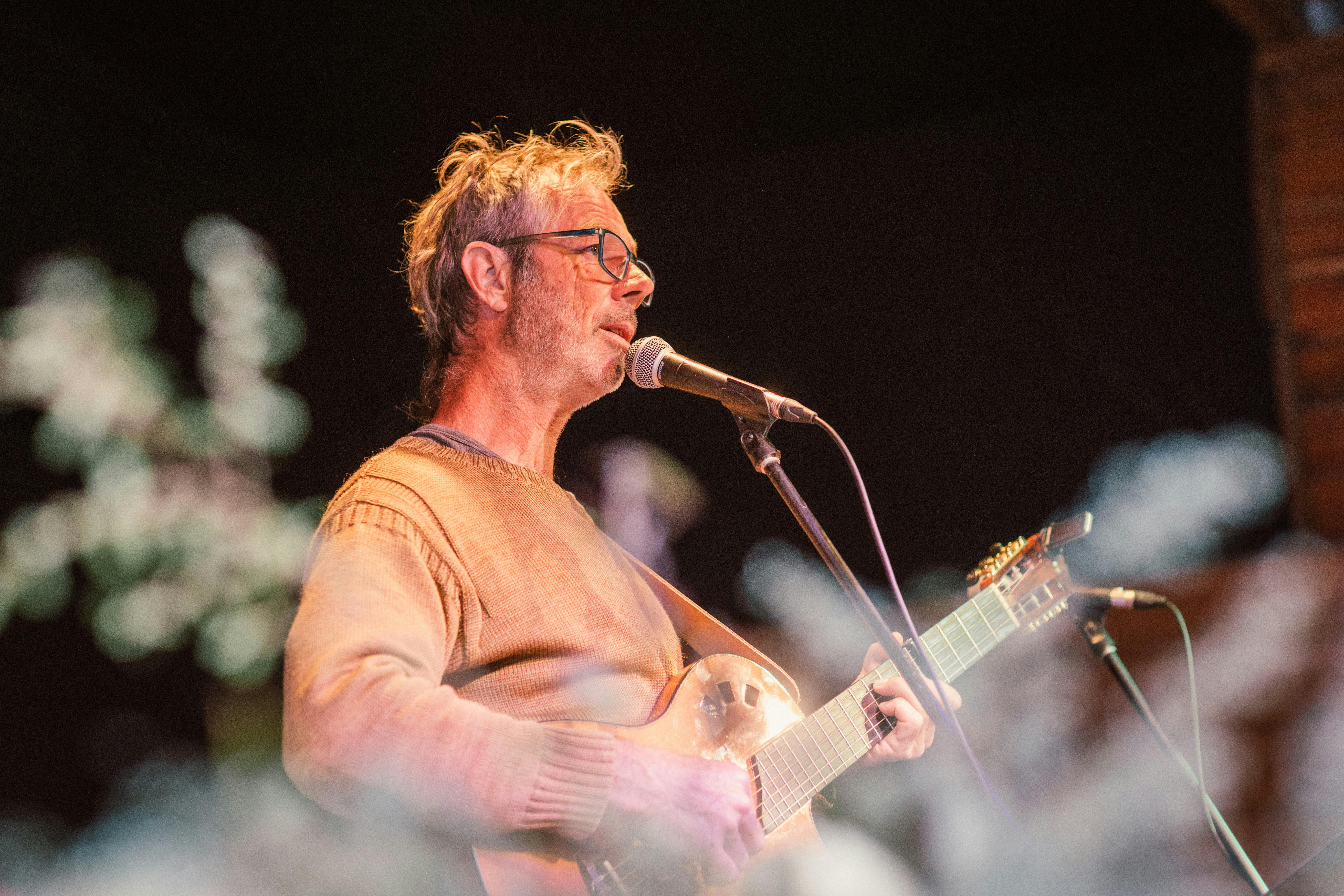 A man is playing guitar and singing with a black background.