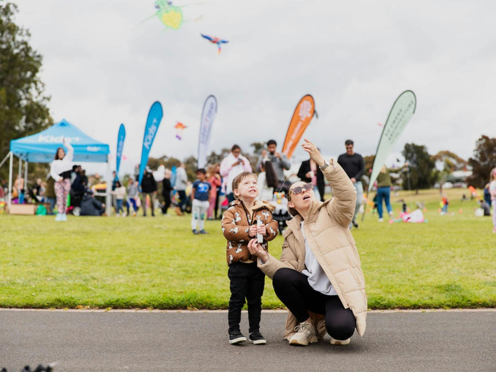A mother points to the sky, showing her young son all the kites as they fly through the sky. ==