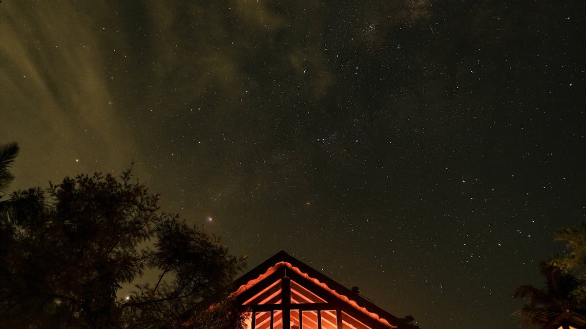 Warmly lit cabin taken from outside at night. Large sky and bright stars.