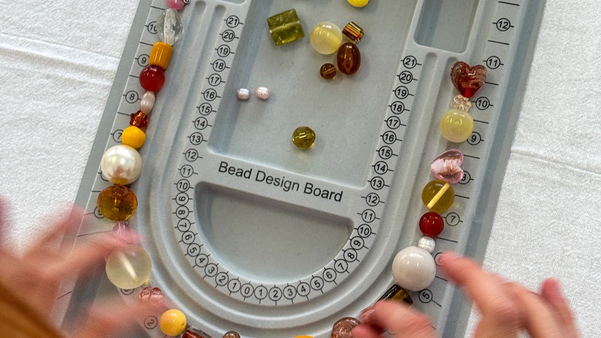A grey bead design board on a table with hands reaching in moving beads around