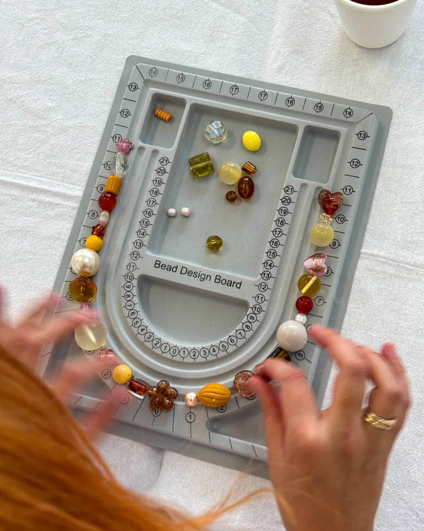 A grey bead design board on a table with hands reaching in moving beads around