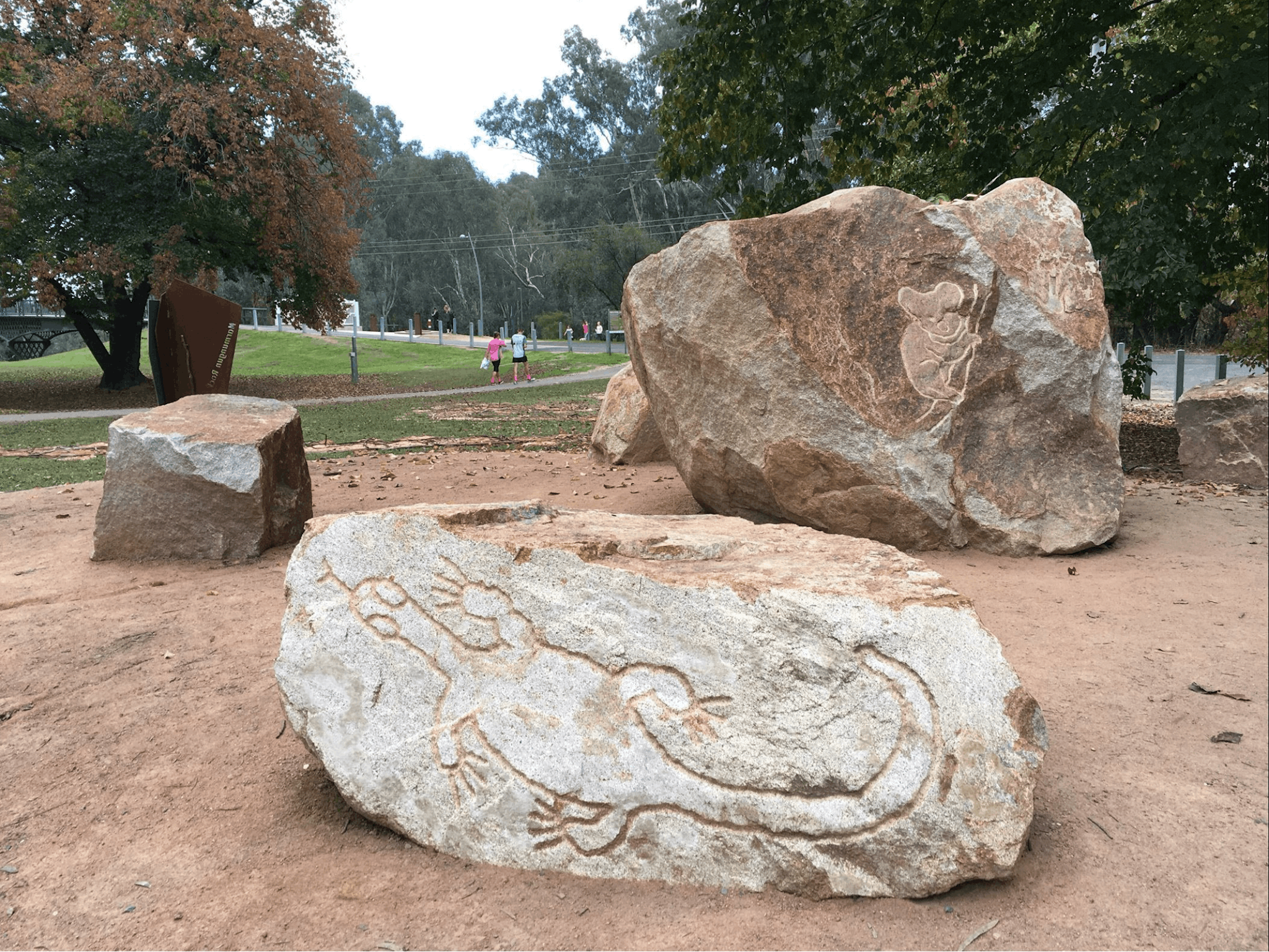 Three large rocks, white rock with carving of lizard, large brown rock with carving of koala,  park