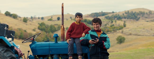 Two young boys lean against a tractor with warm smiles.