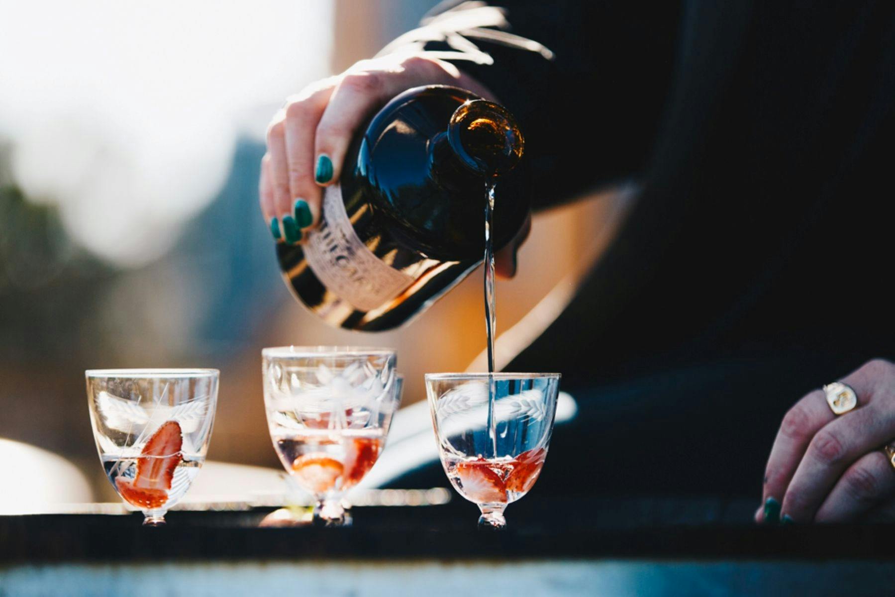 Gin being poured into cocktail with strawberry garnish