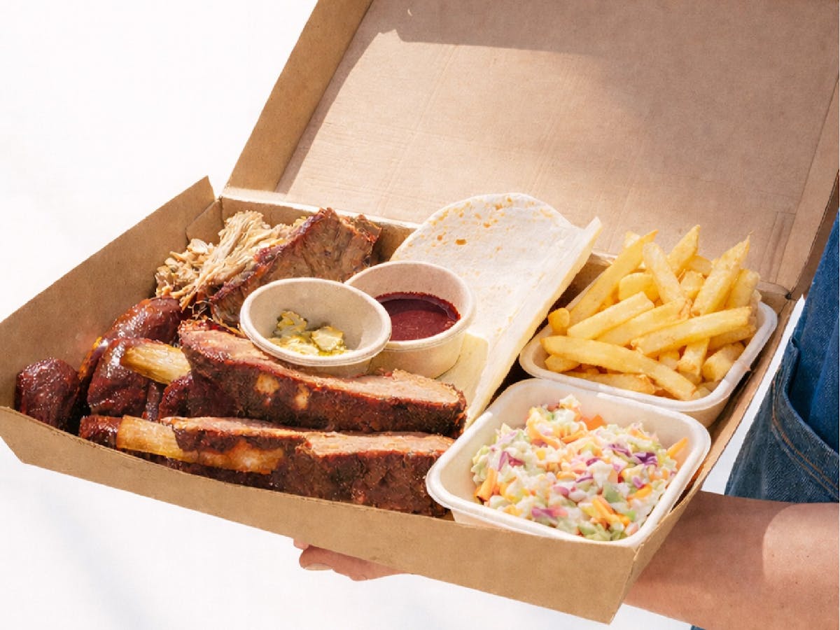 Smoked BBQ share platter with brisket, beef ribs, pulled pork, fries, coleslaw, pickles served a box