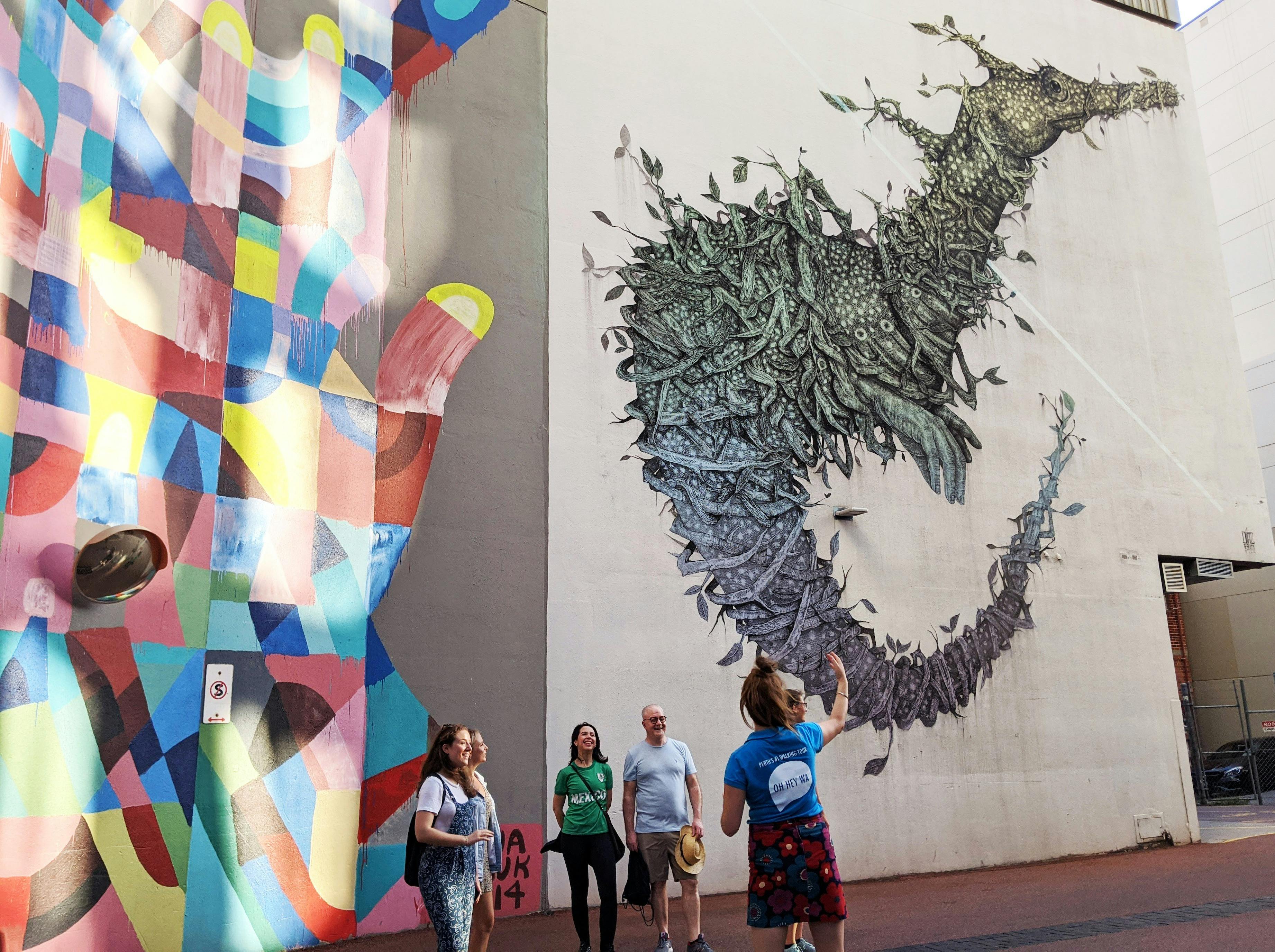 A tour guide a guests standing in front of some large murals