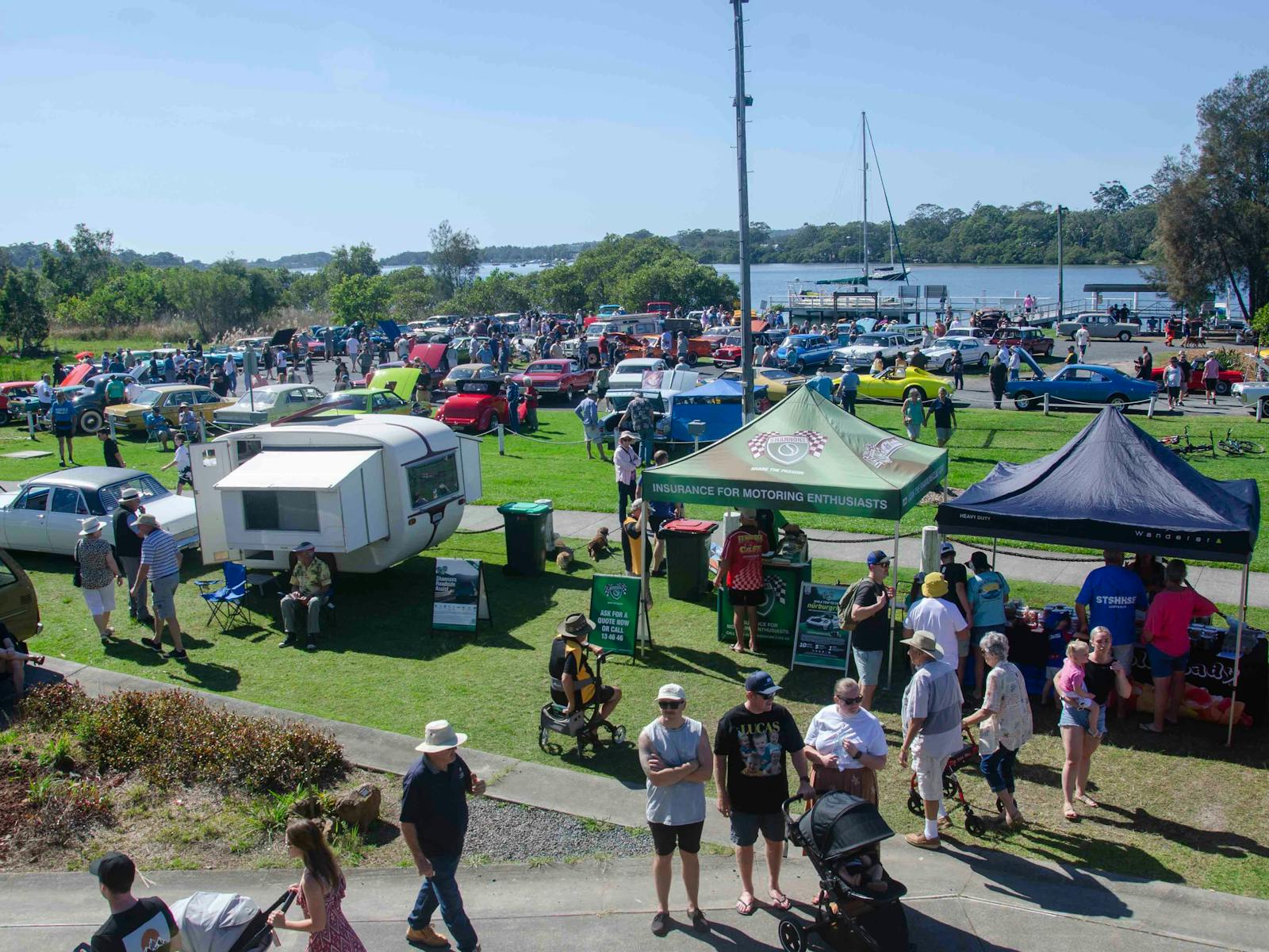 View towards river with classic cars and spectators in foreground, 2024